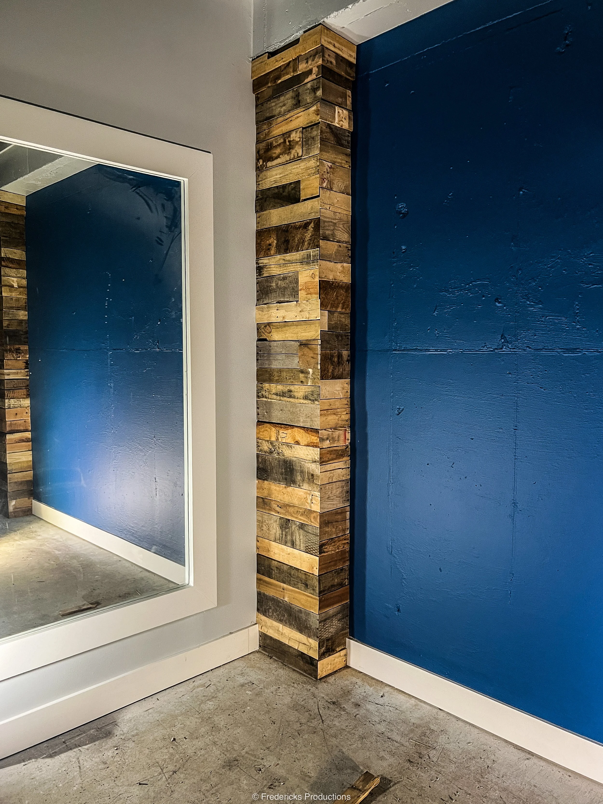Interior corner with a blue wall, a mirror, and a decorative wooden column.