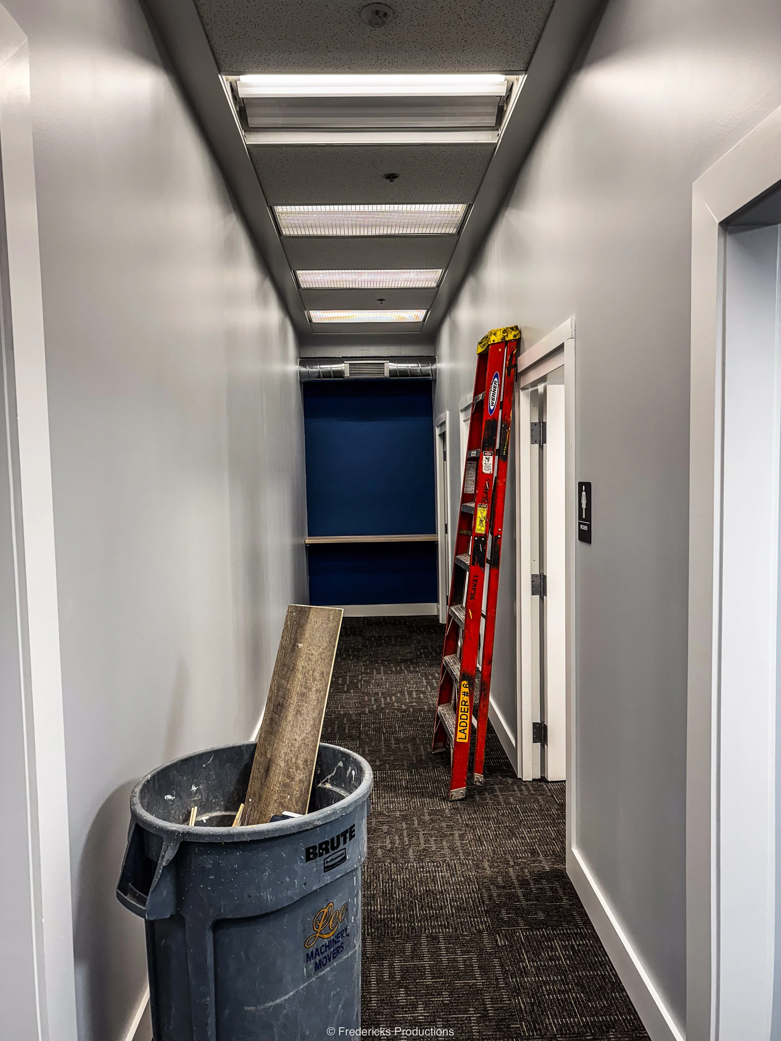 A construction or maintenance hallway with a trash can, ladder, and some construction tools and materials.
