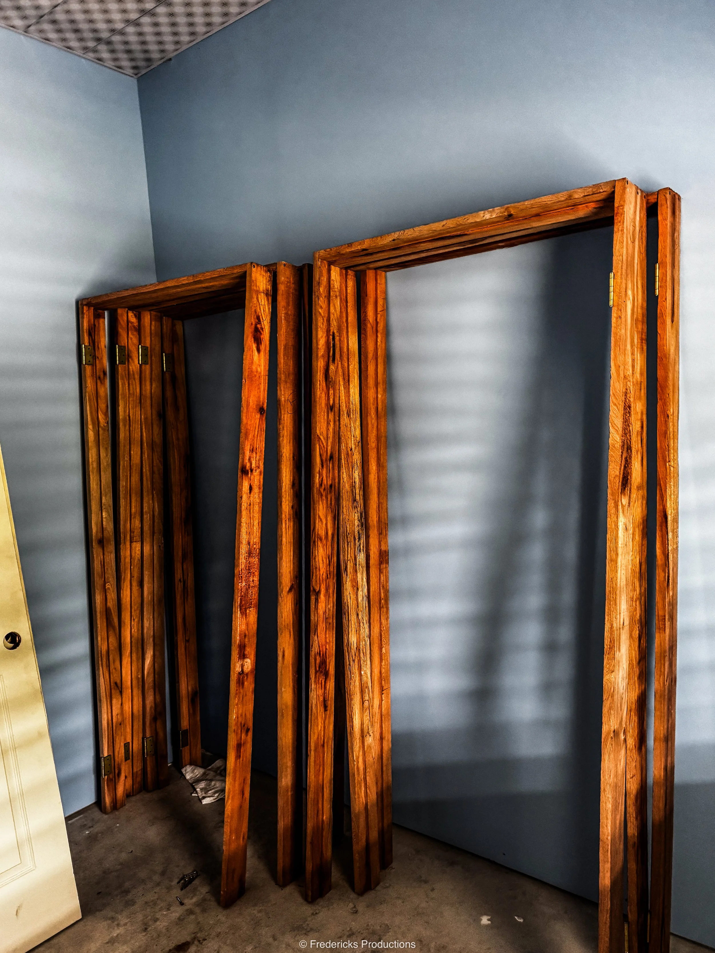 Unassembled wooden door frames leaning against a light blue wall in a room under construction.
