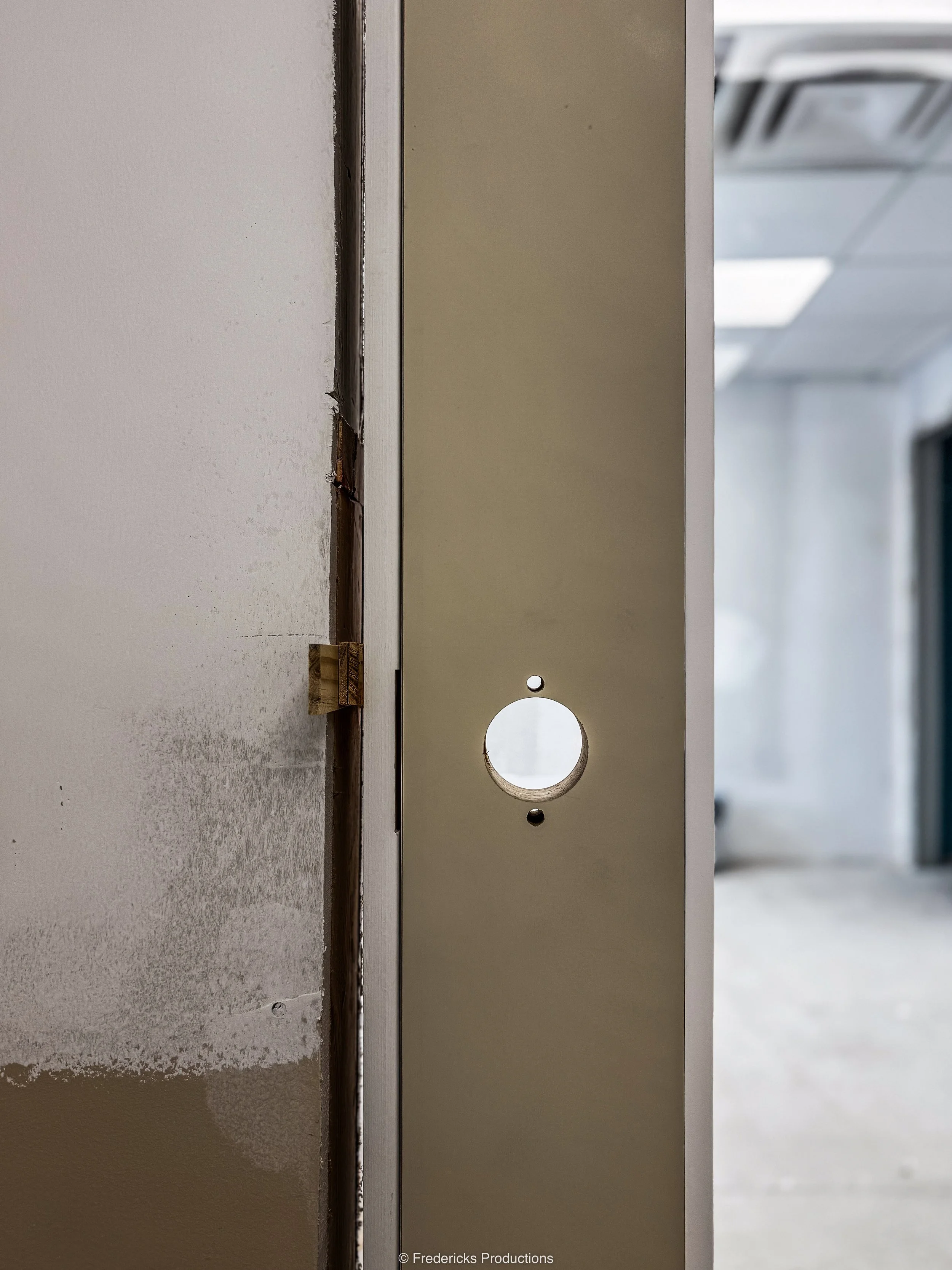 Close-up of a metal mounting plate with a circular cutout, attached to a partially finished wall in a construction site.