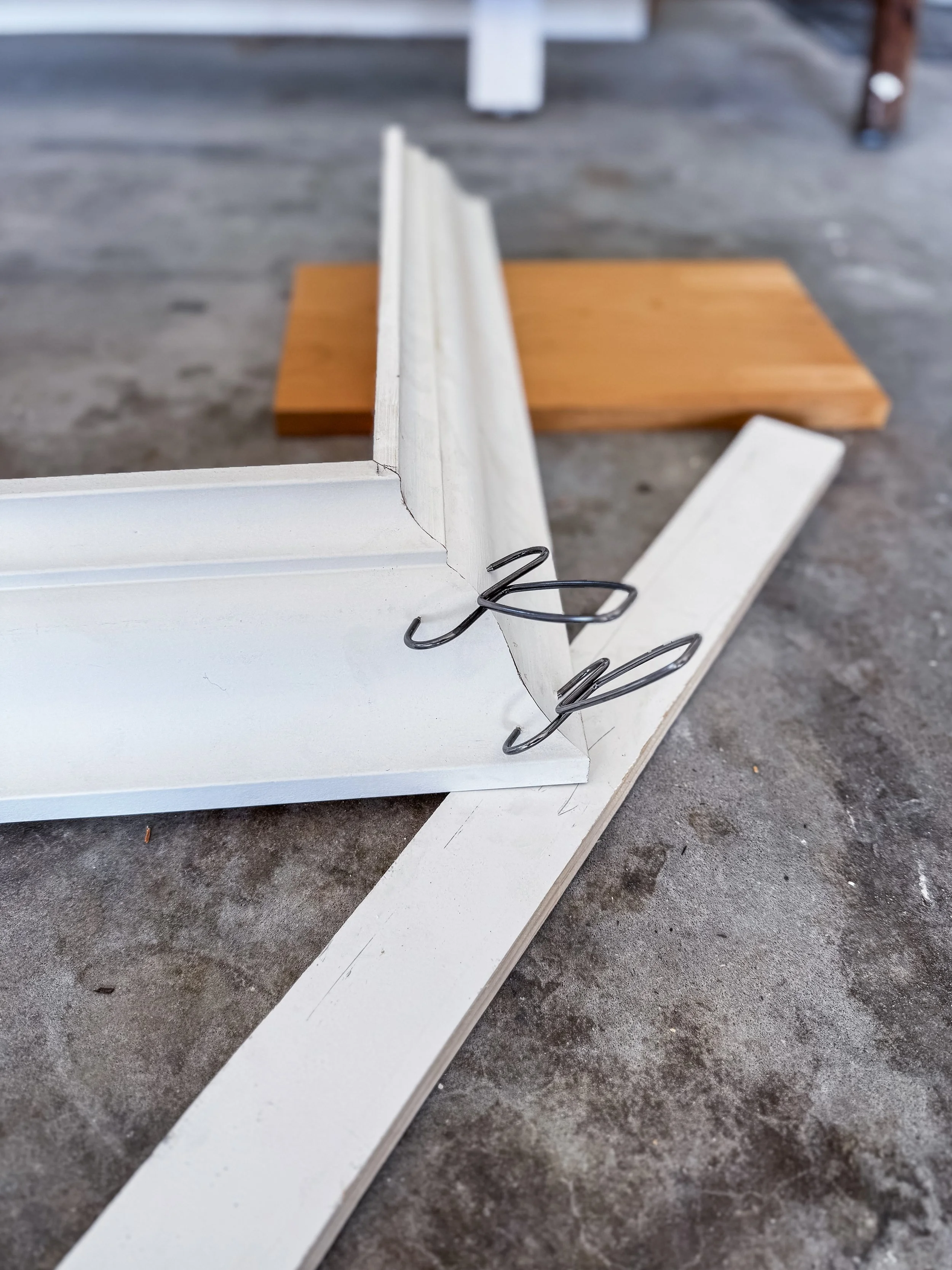 Close-up of a white crown molding piece with metallic spring clip attached, placed on a concrete floor