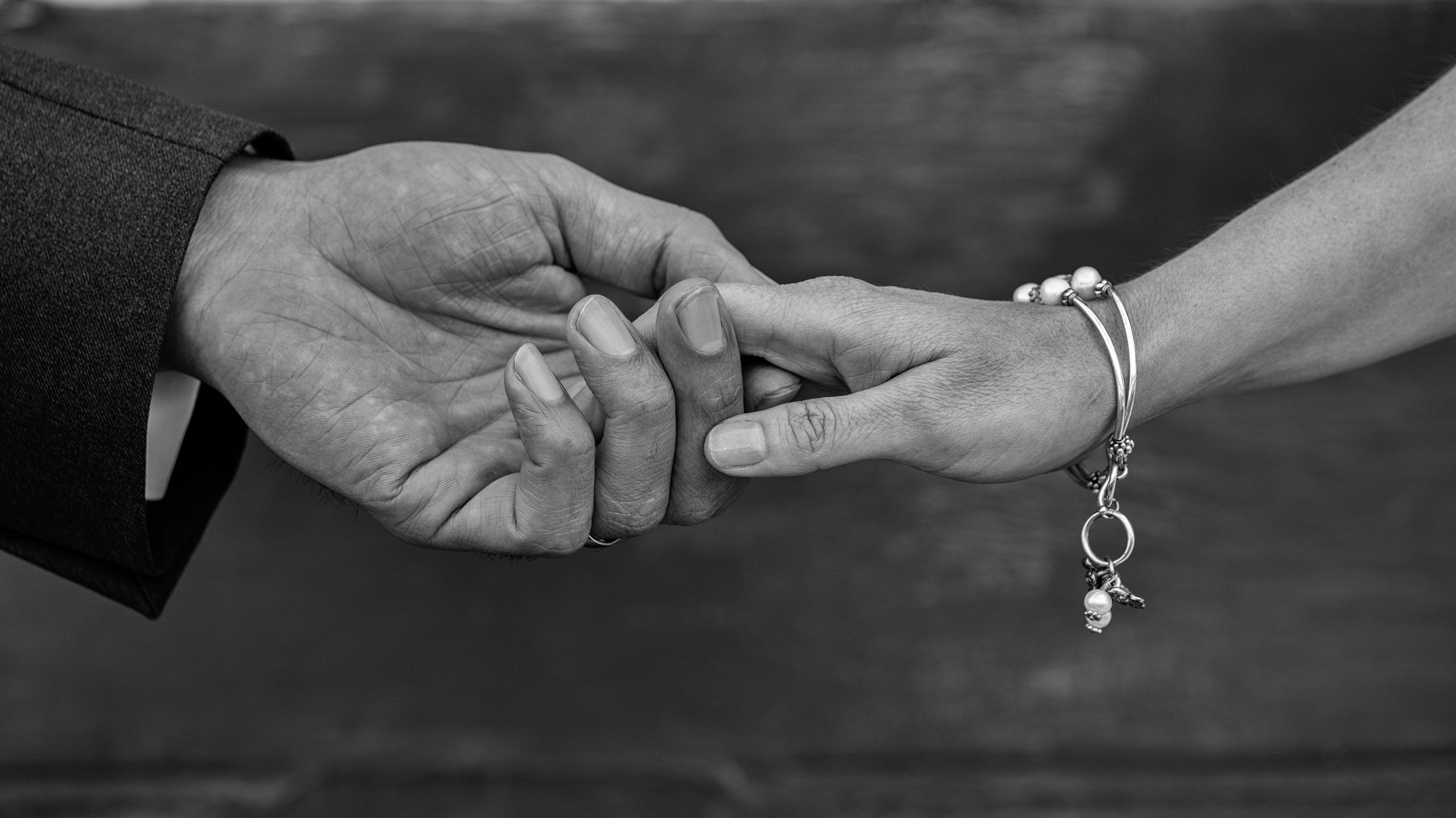 Two hands holding each other, one with a darker skin tone and the other with a lighter skin tone, on a wooden surface.