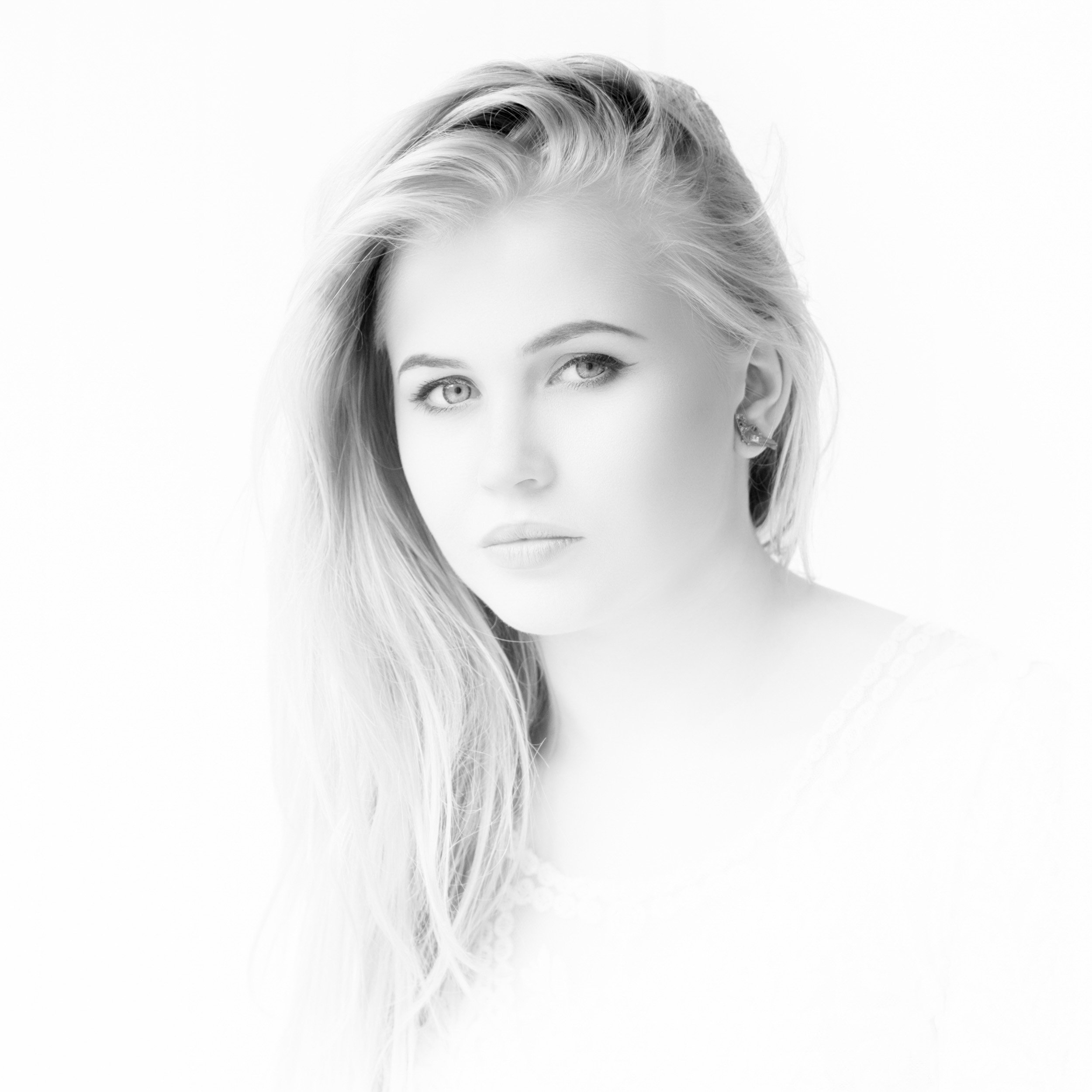 A low key black-and-white portrait of a young woman with long, wavy hair looking at the camera with a neutral expression.