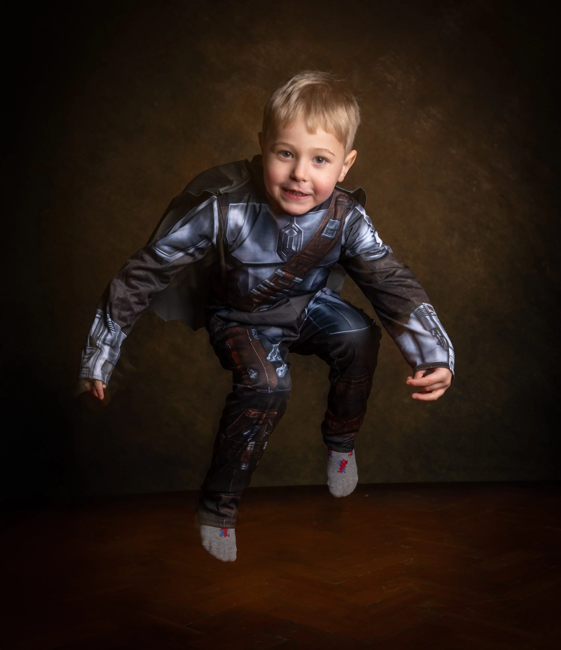 A young boy dressed in a Star Wars-themed outfit, jumping with a playful expression, on a dark background.