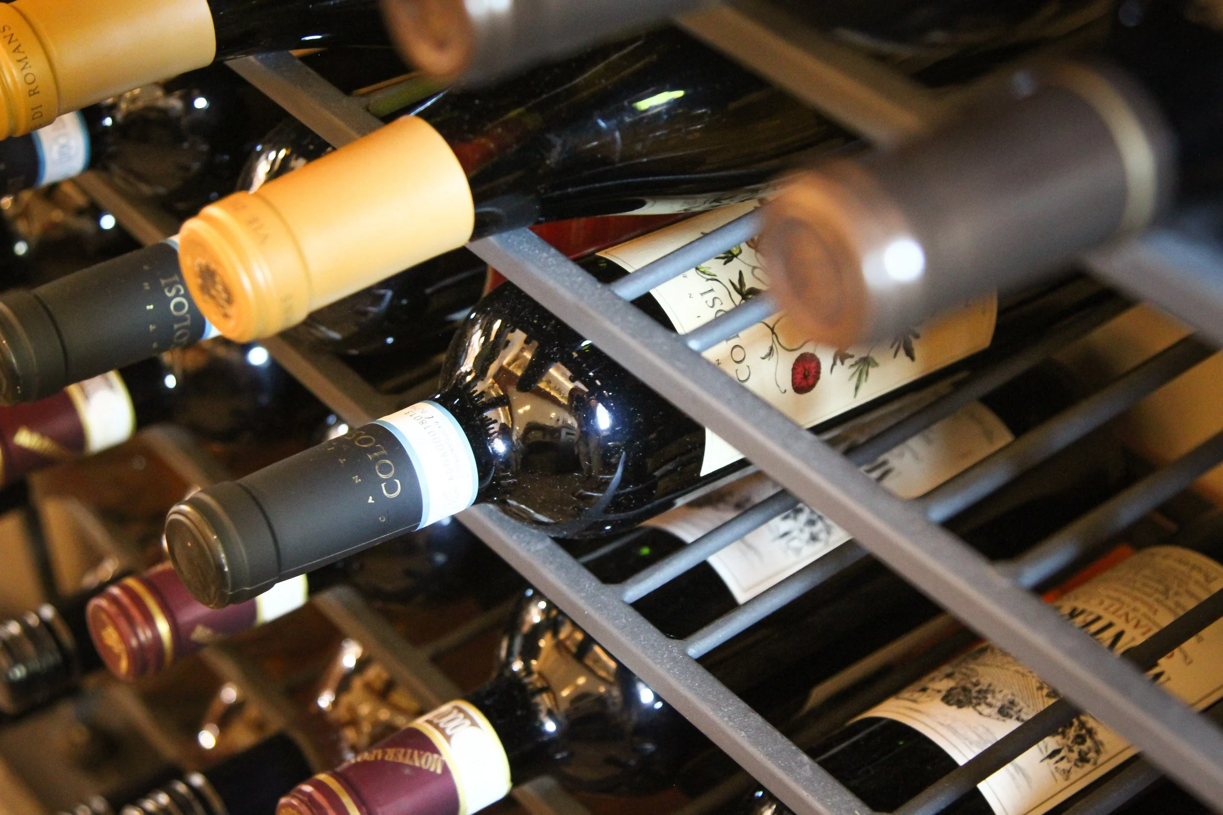 A close-up view of wine bottles stored on a metal wine rack, with some bottles showing labels and others turned sideways.