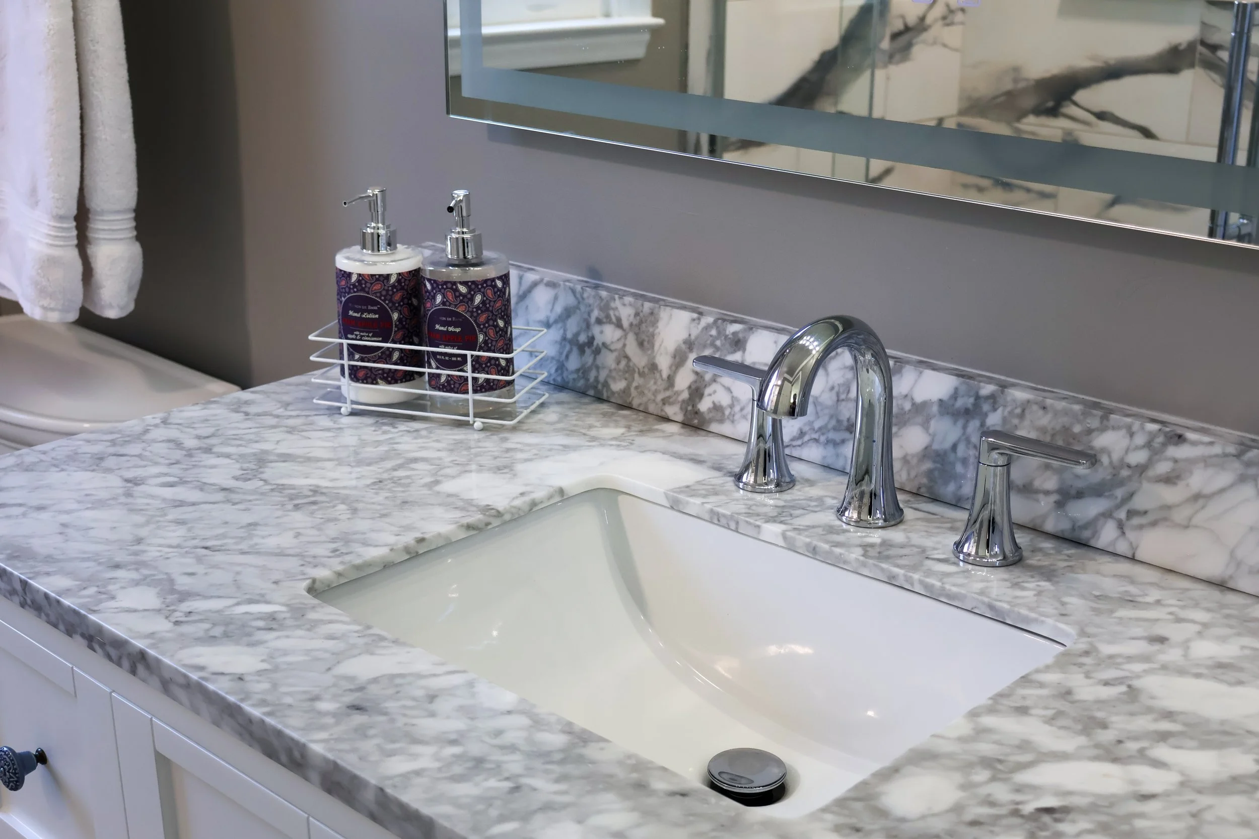 Bathroom sink with a marble countertop, two soap dispensers, a faucet, and a mirror above.