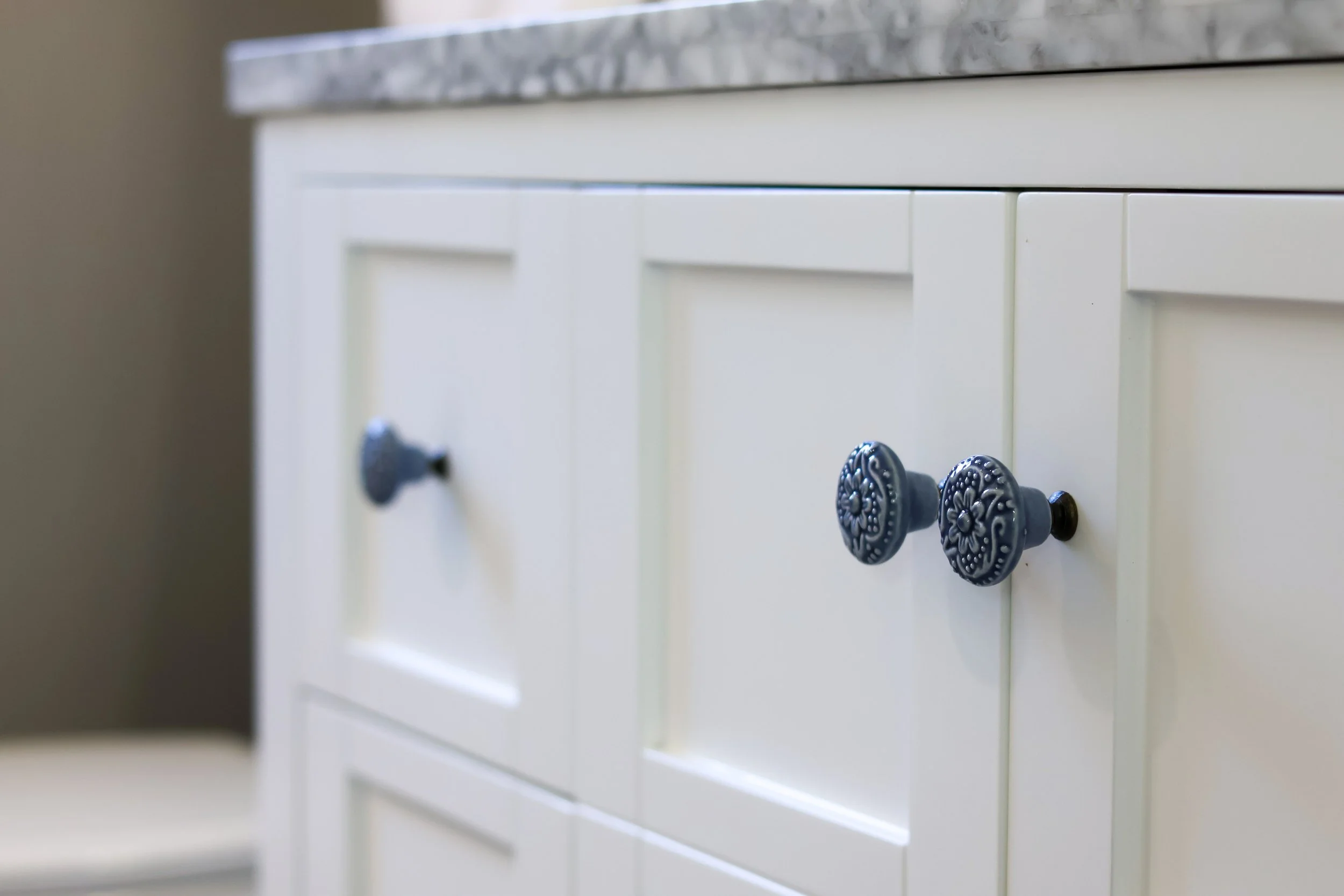 A white kitchen cabinet with decorative blue handles and a gray marble countertop.