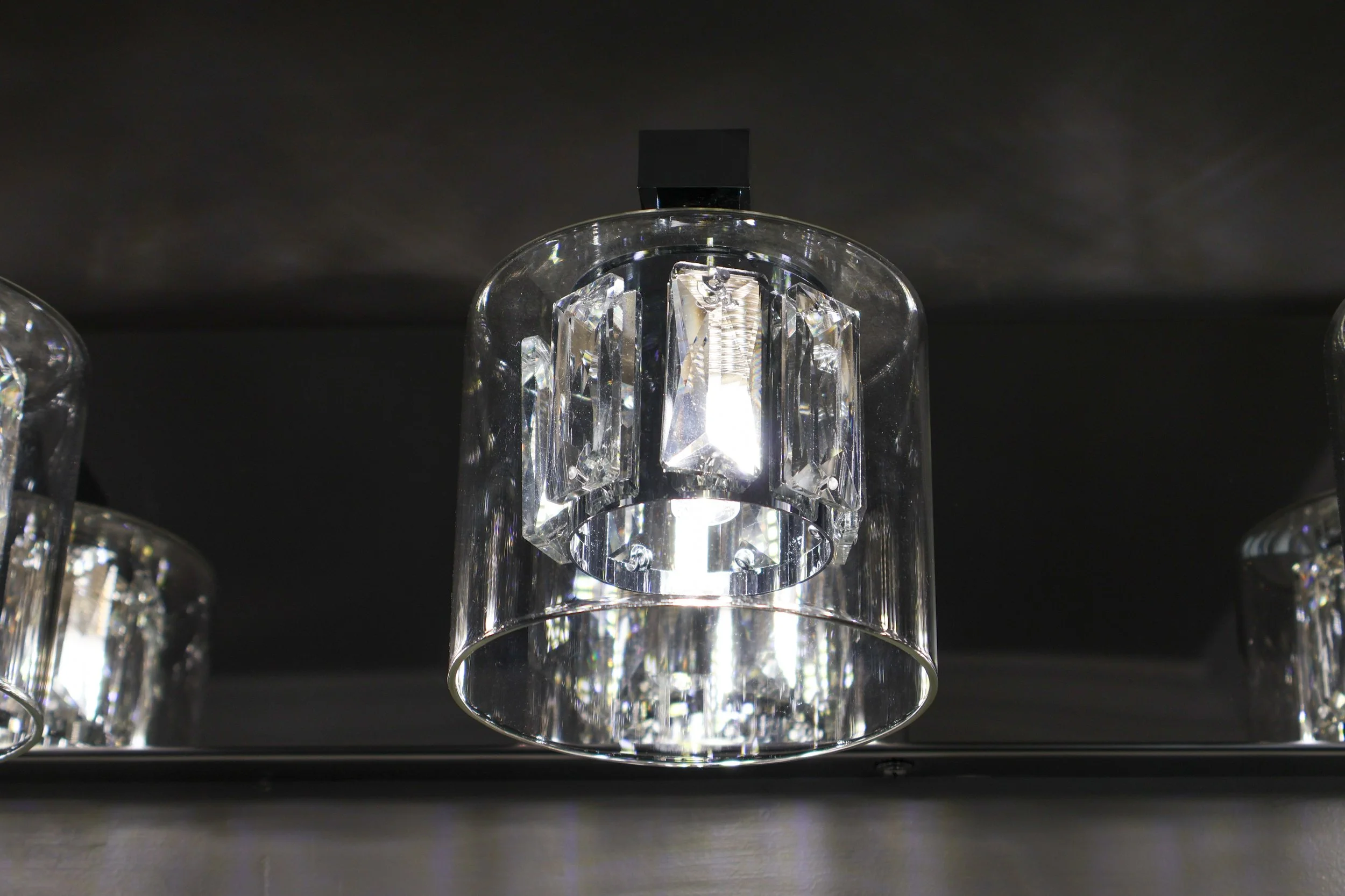 Close-up of a modern ceiling light fixture with a cylindrical glass shade and decorative crystal accents, mounted on a black ceiling.