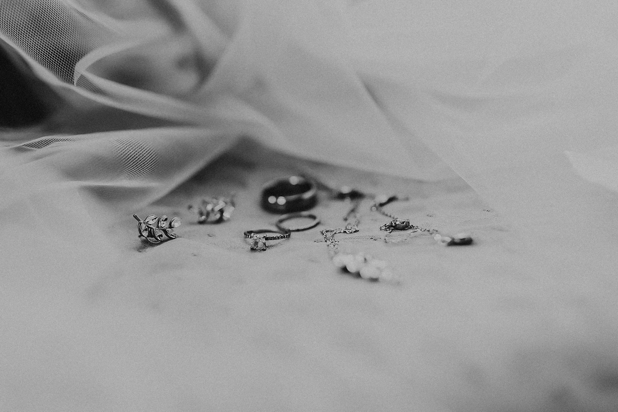 Various jewelry pieces, including rings and earrings, spread out on a soft surface with a fabric backdrop.