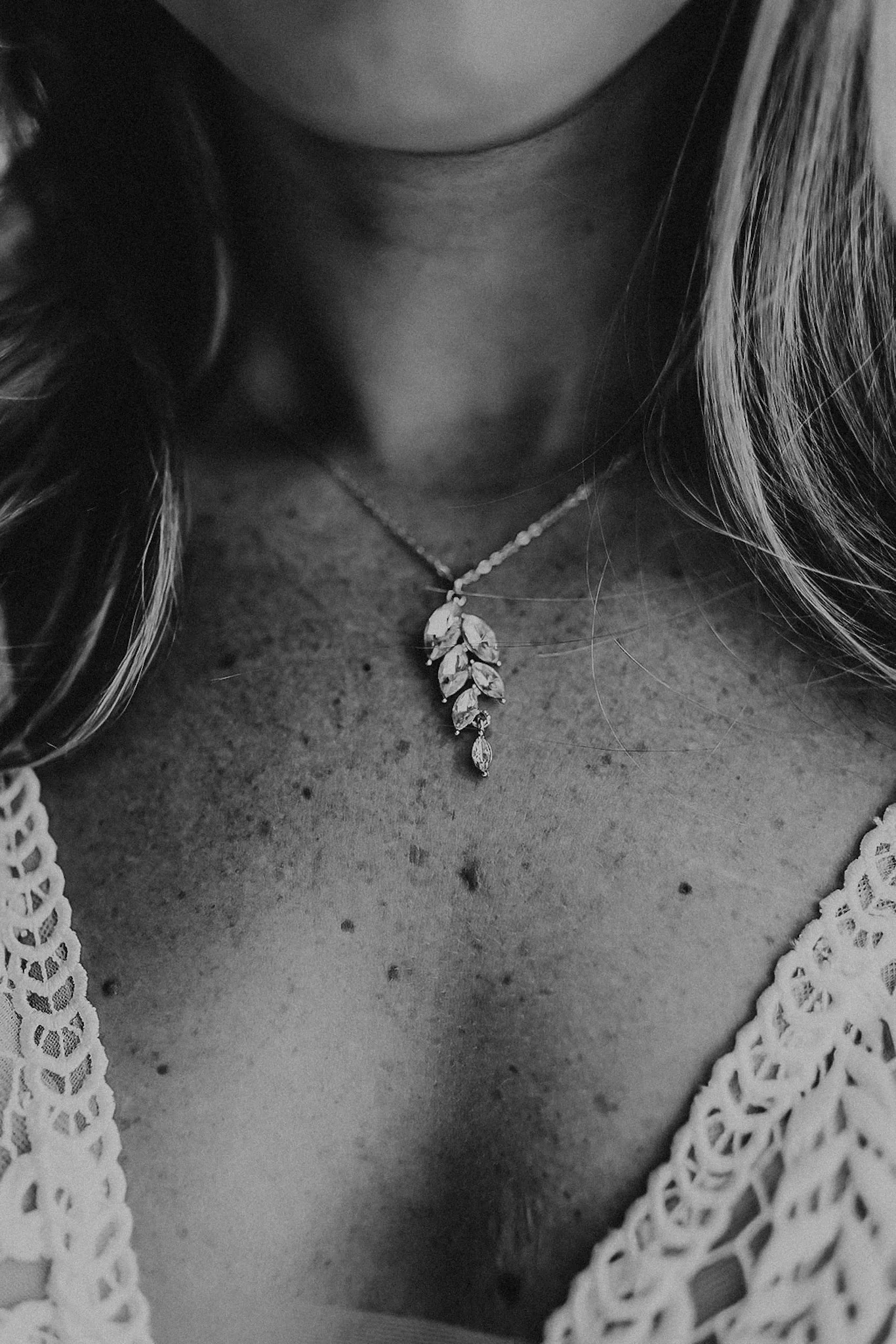 Close-up of a woman's neck and upper chest, showing a leaf-shaped pendant necklace and a lace top.