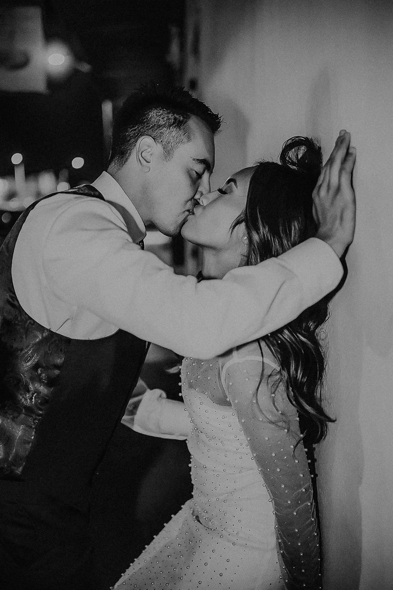 A black and white photo of a man and woman kissing, with the man holding the woman's face against the wall.