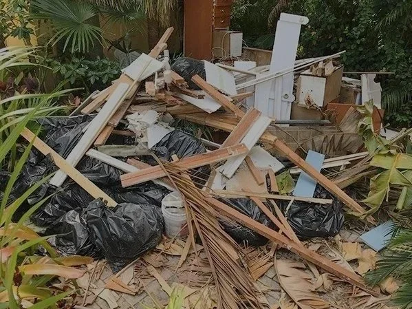 Pile of scattered debris including wood scraps, black trash bags, and household items outdoors