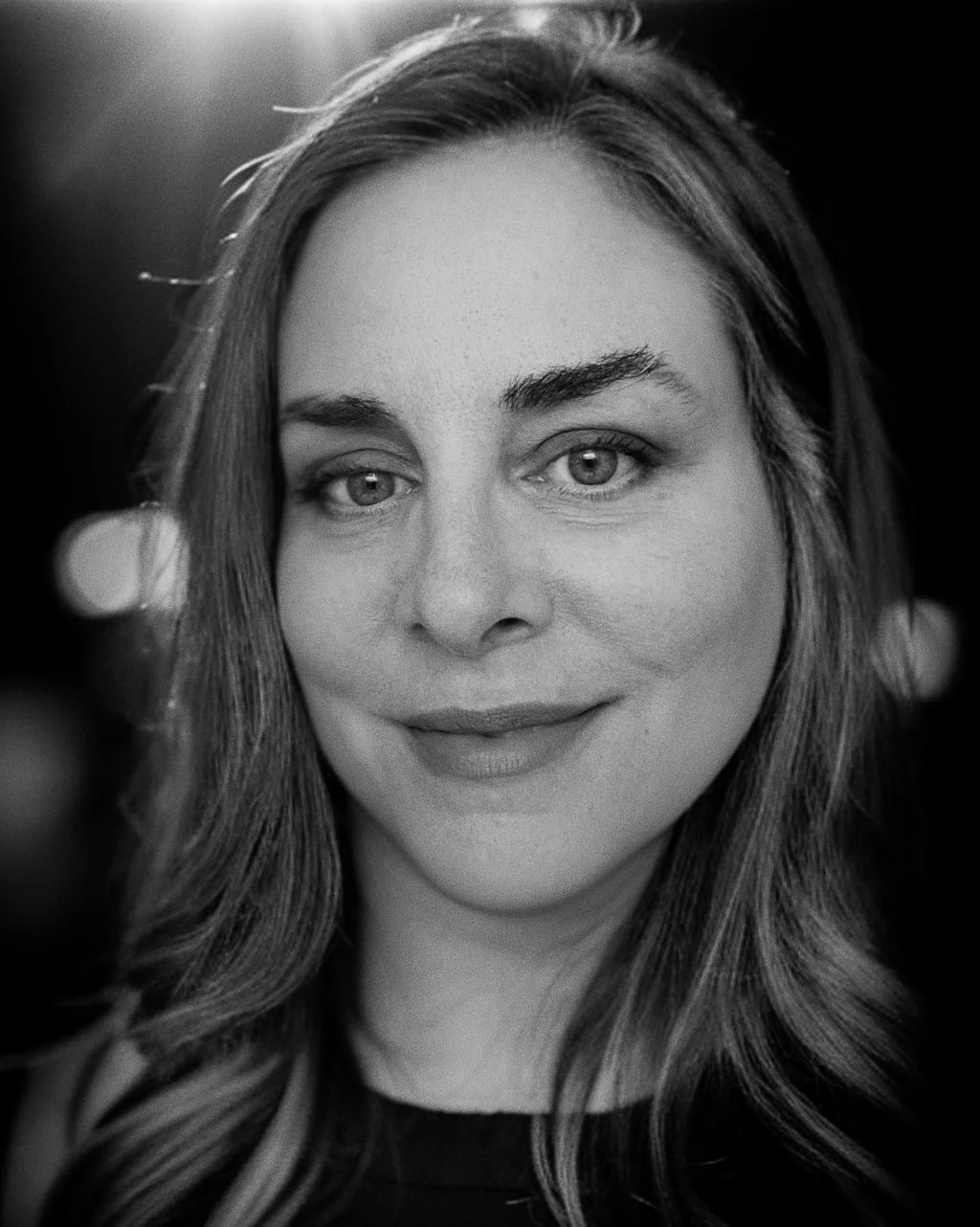 Close-up black and white photograph of a smiling woman with wavy hair, looking at the camera.