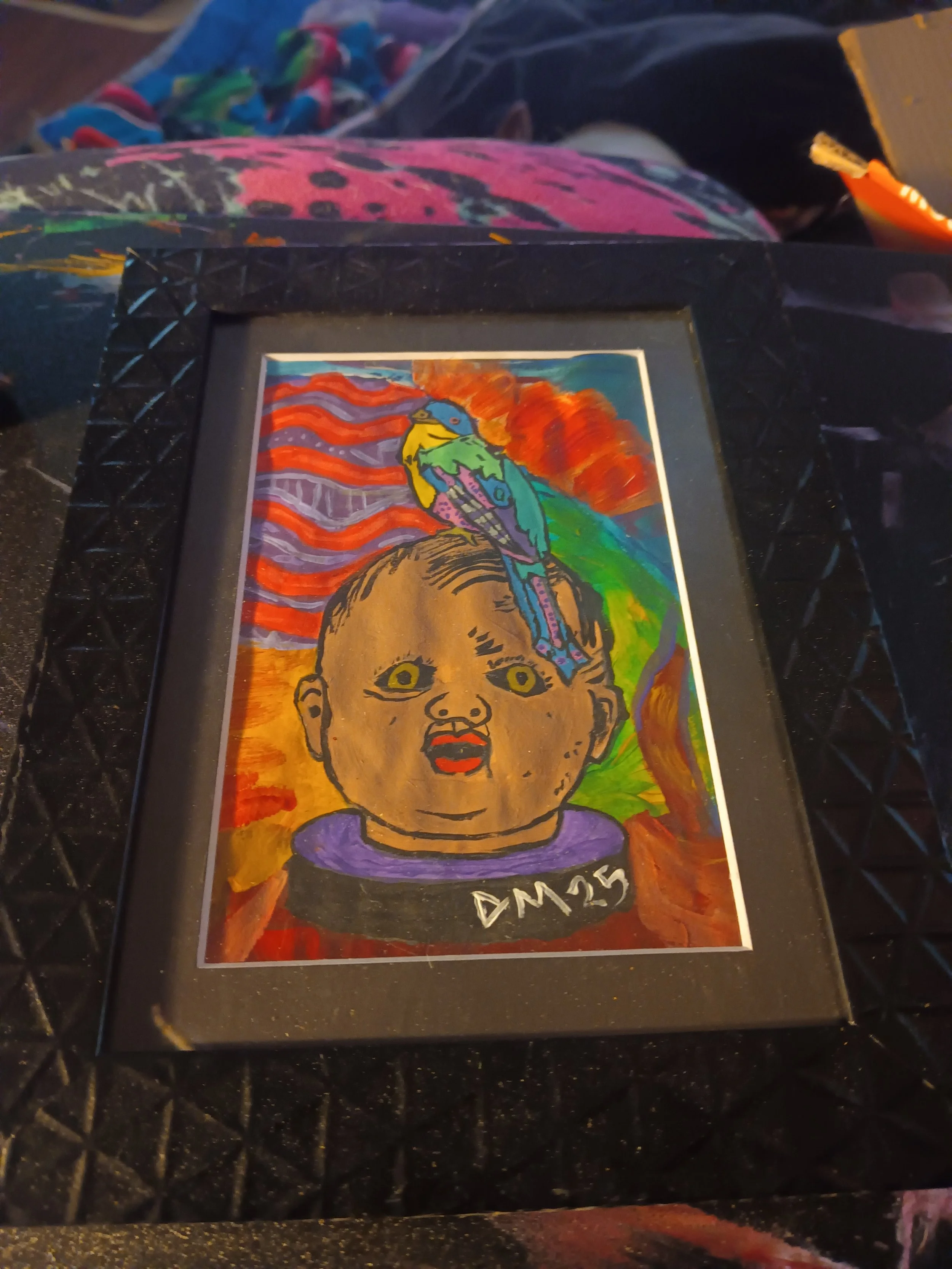 Colorful illustration of a baby with exaggerated facial features, including large eyes and lips, wearing a black collar with white letters 'DM25'. A vibrant background with swirling colors and a bird perched on the baby's head.