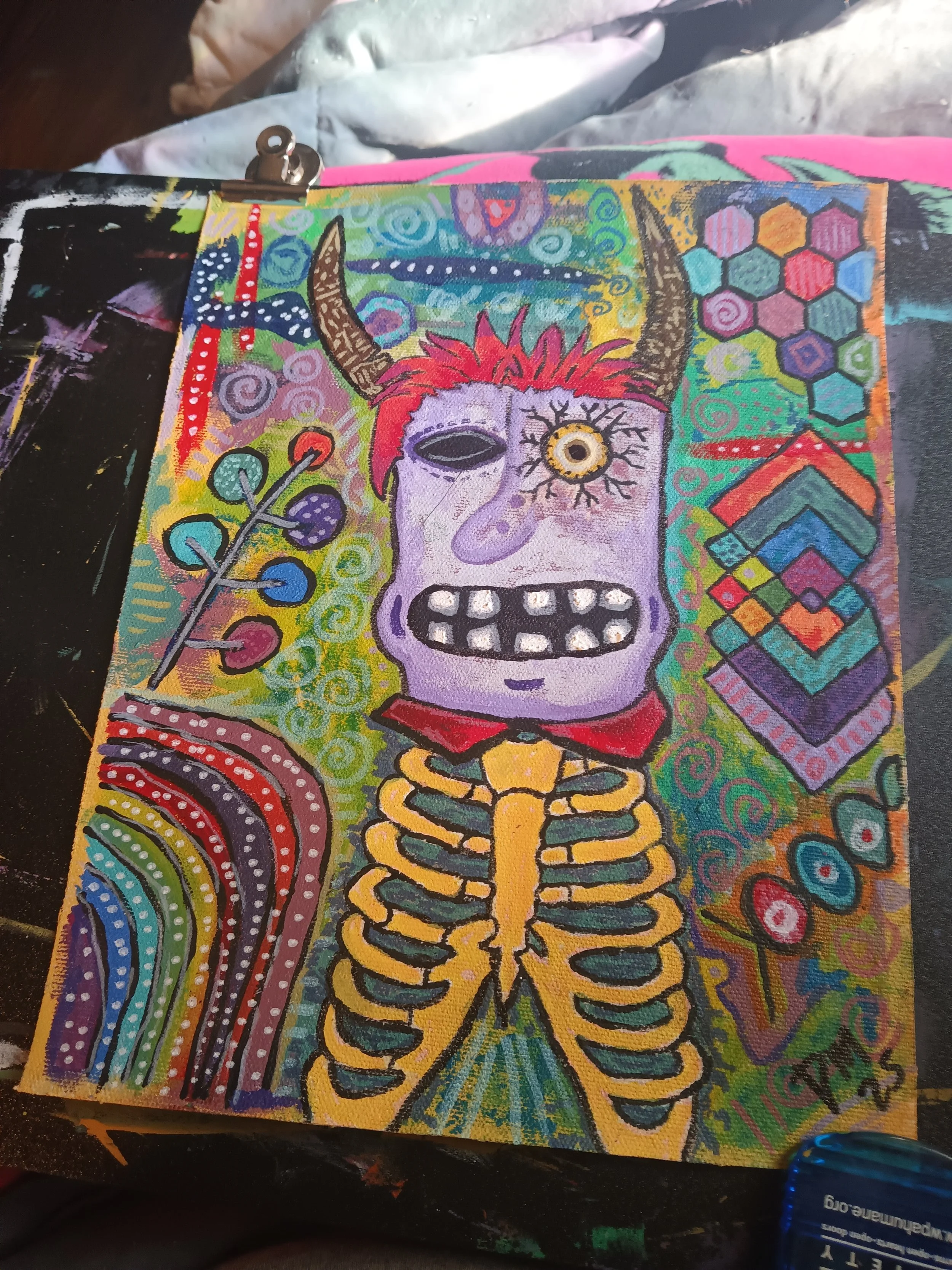 Colorful abstract painting of a skeletal creature with horns, one eye, red hair, and a wide-open mouth, surrounded by vibrant patterns and geometric designs.