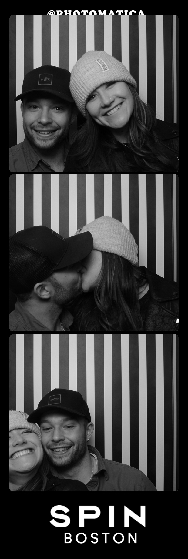 Three black and white photo booth images of a smiling young couple with a striped background. In the first image, they are standing close, smiling; the woman wears a beanie and the man a cap. In the second image, they are kissing, with the man wearing a cap and the woman wearing a beanie. In the third image, they are smiling together, with the woman also wearing a beanie. The bottom of the image has the text "SPIN BOSTON."