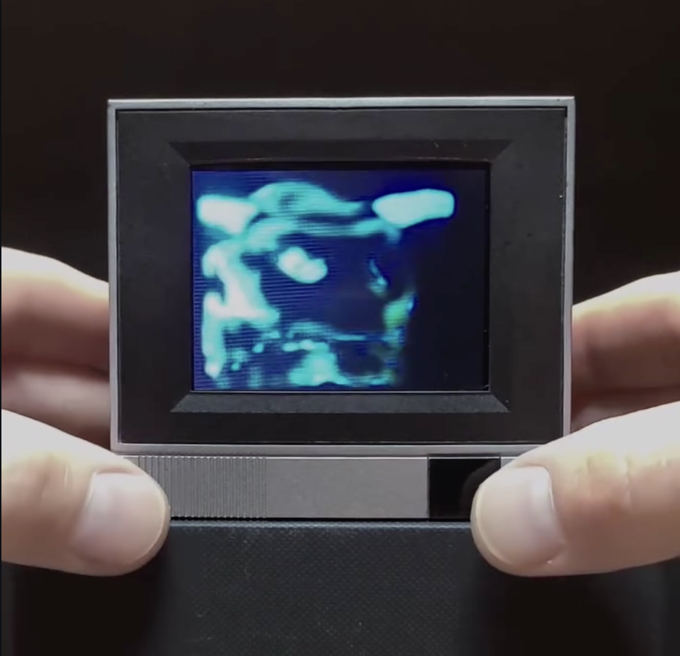 Fingers holding a small digital screen, displaying a hyperealistic 3D ultrasound image of a baby.