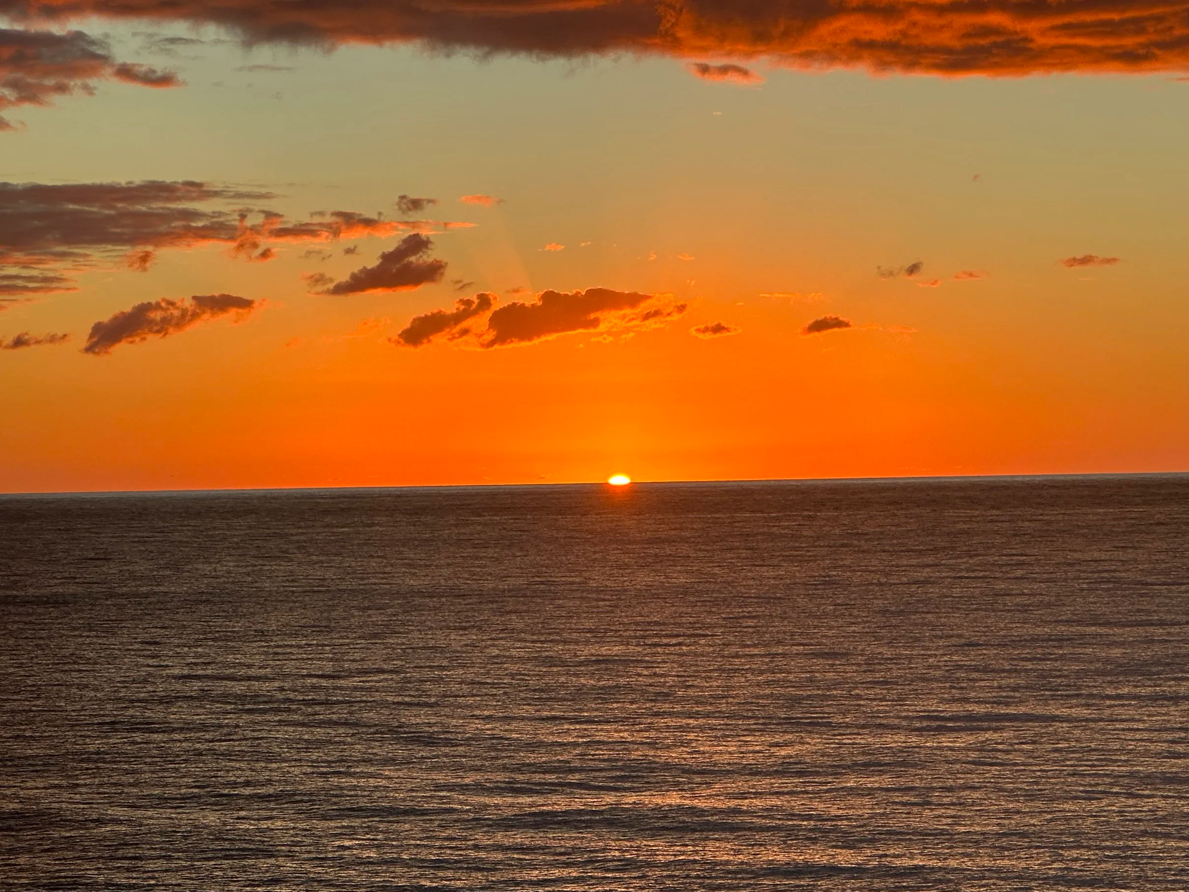 Sunset over the ocean with a few clouds in the sky.