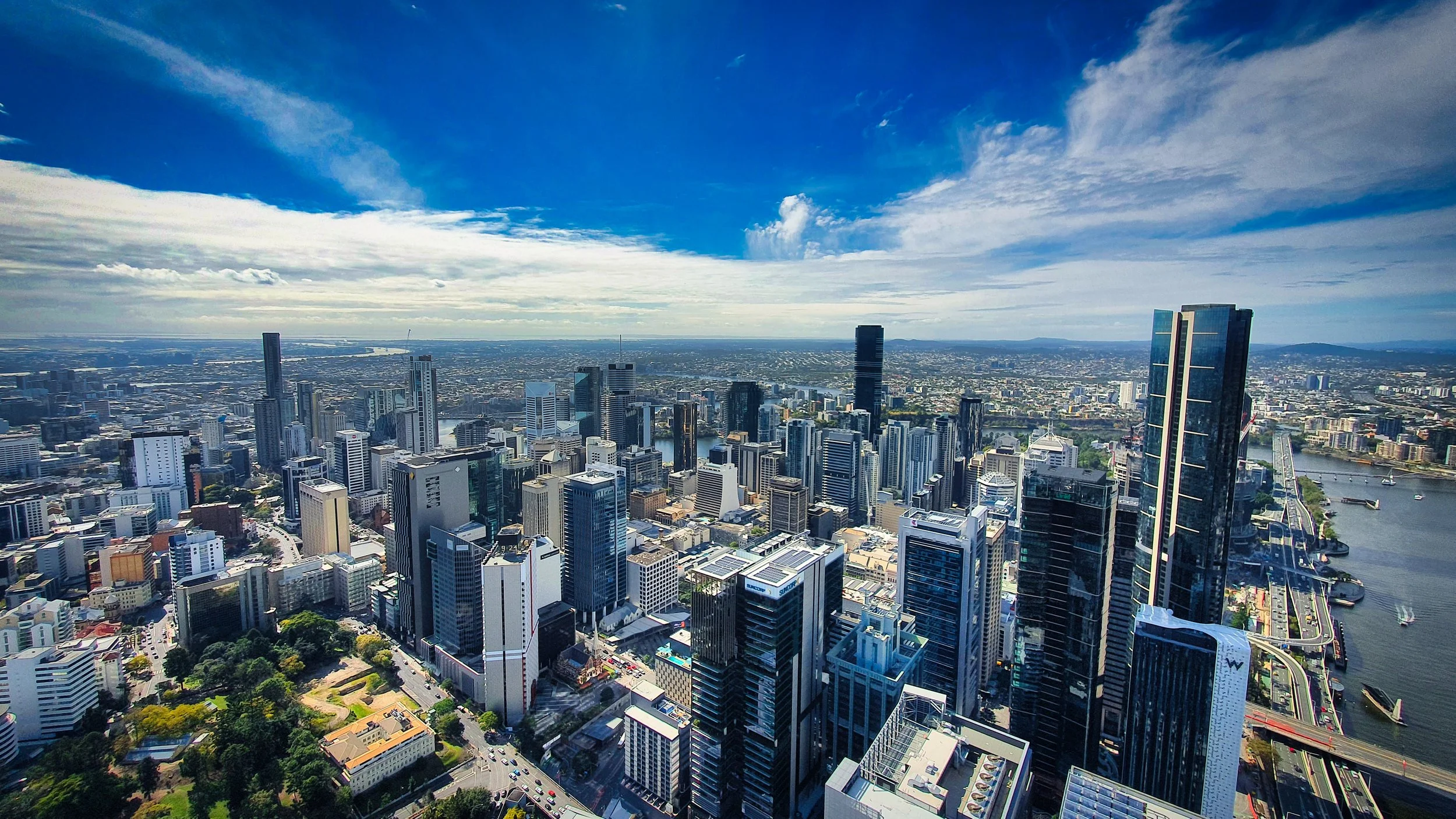 Aerial view of a city skyline with many tall skyscrapers along a river, under a partly cloudy blue sky.