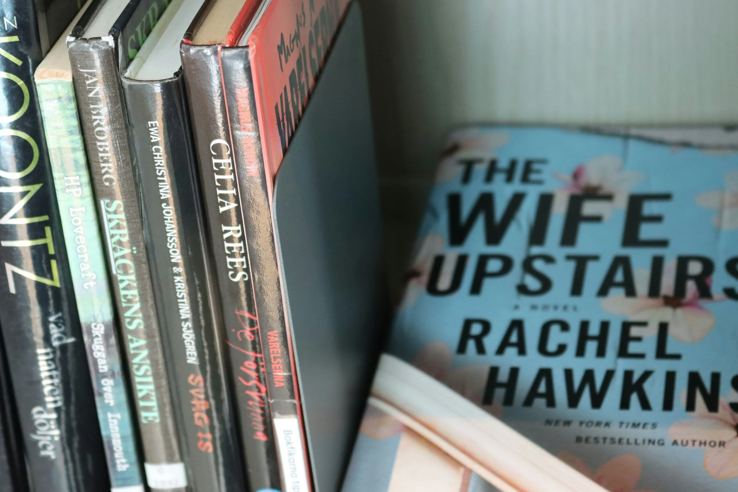 Shelf of books, including 'The Wife Upstairs' by Rachel Hawkins and several books with partially visible titles.