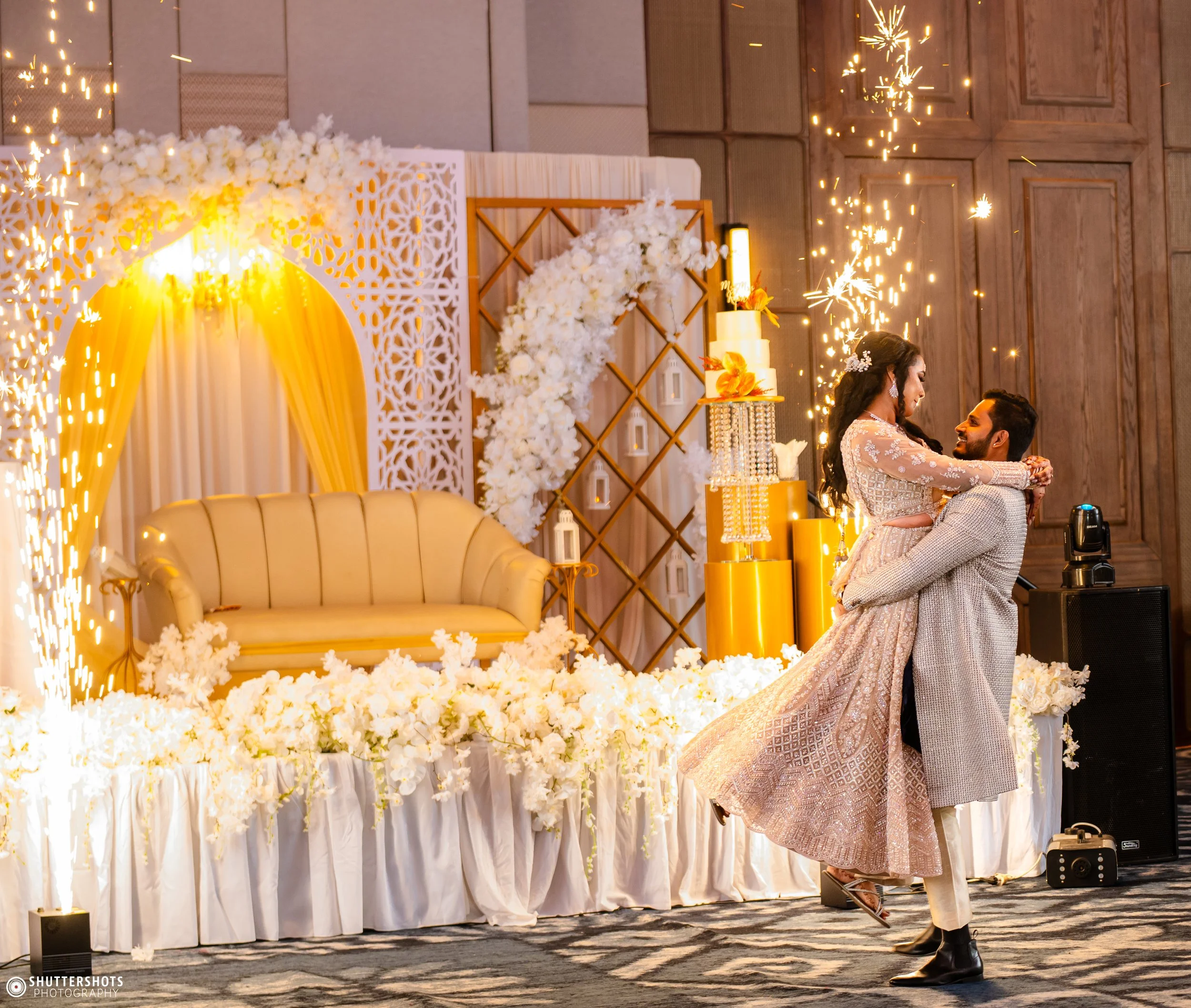 A couple dancing at their wedding reception with fireworks, floral decorations, a cake, and a decorative porch