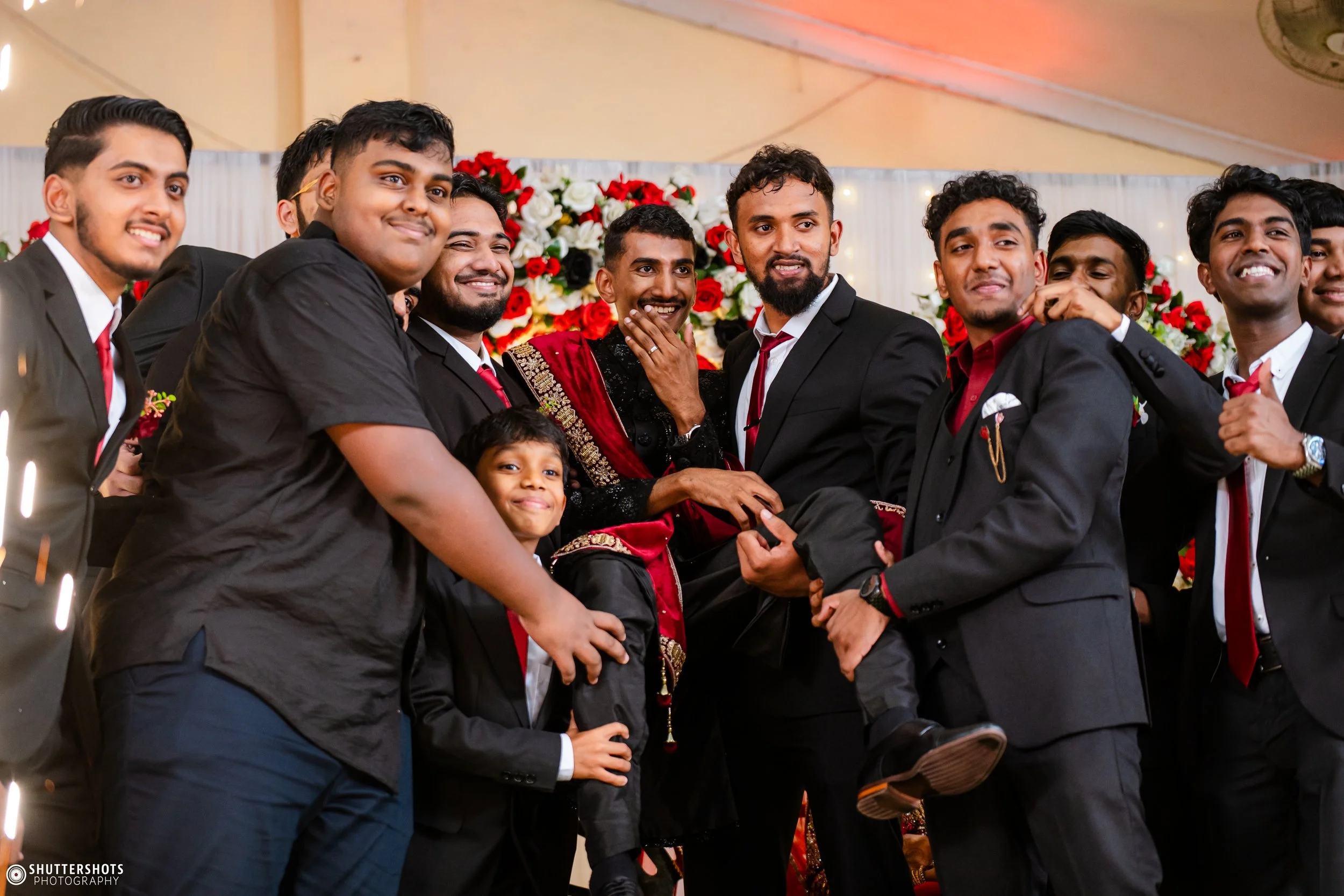 Group of men and a boy dressed in formal attire at a celebration, with a floral backdrop.