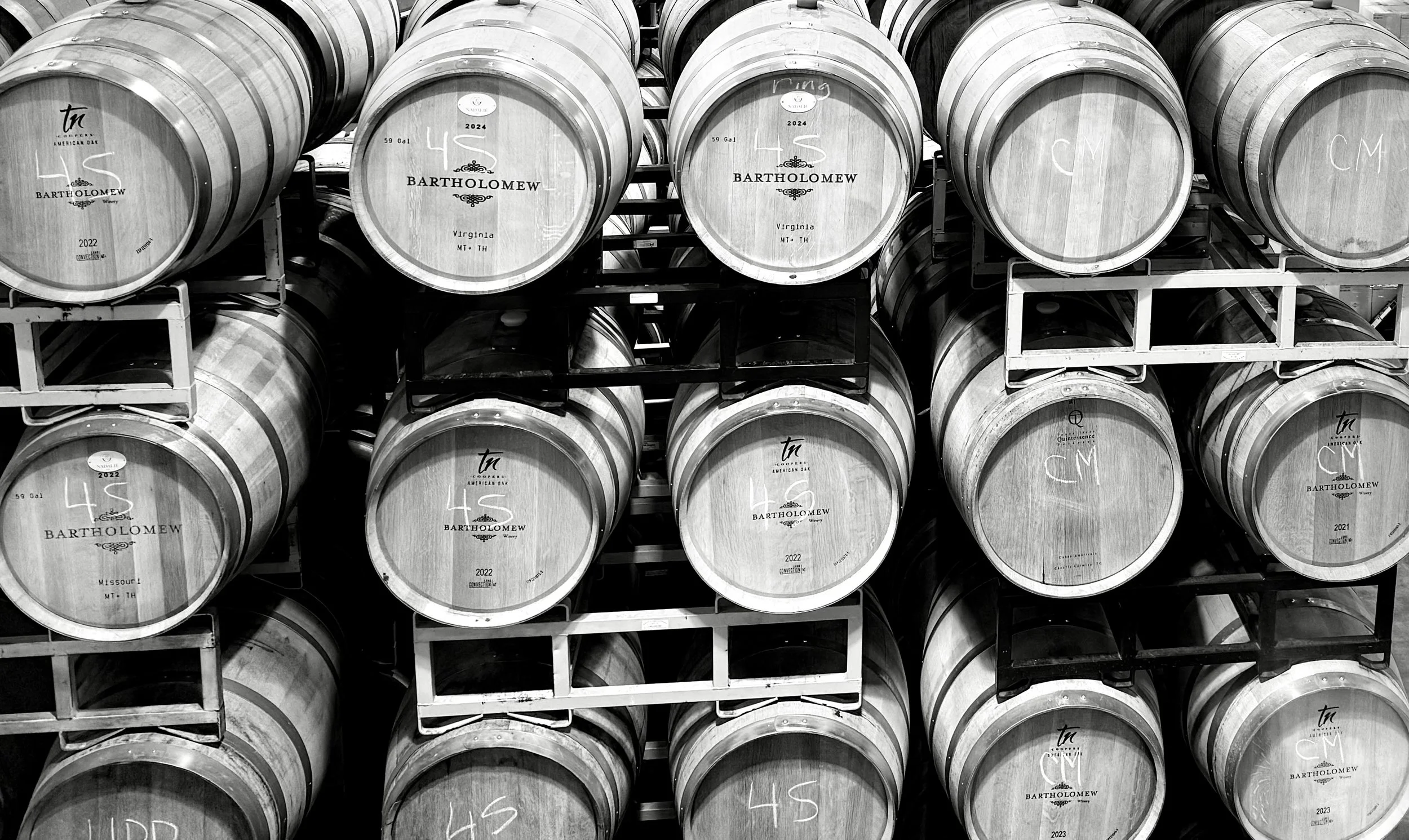 Black and white atmospheric shot of the rustic barrel room at Bartholomew Winery, the heart of our Washington winemaking experience.