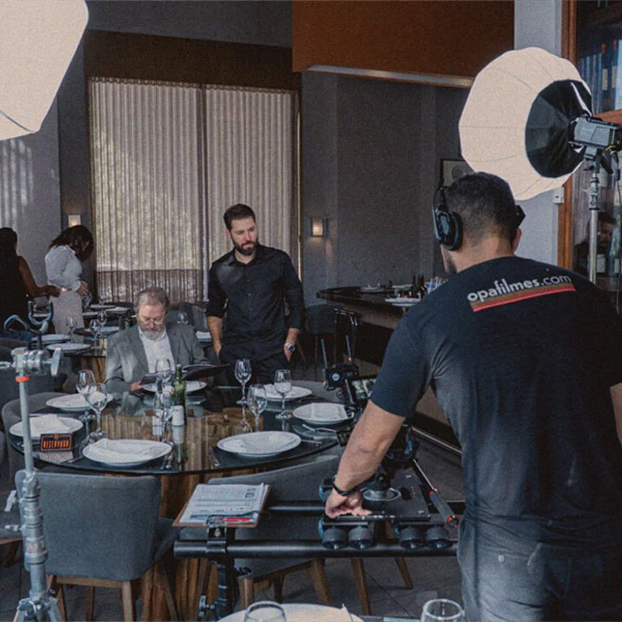 Equipe de filmagem ajustando equipamento de iluminação em um restaurante com mesa posta para uma sessão de fotos ou gravação.