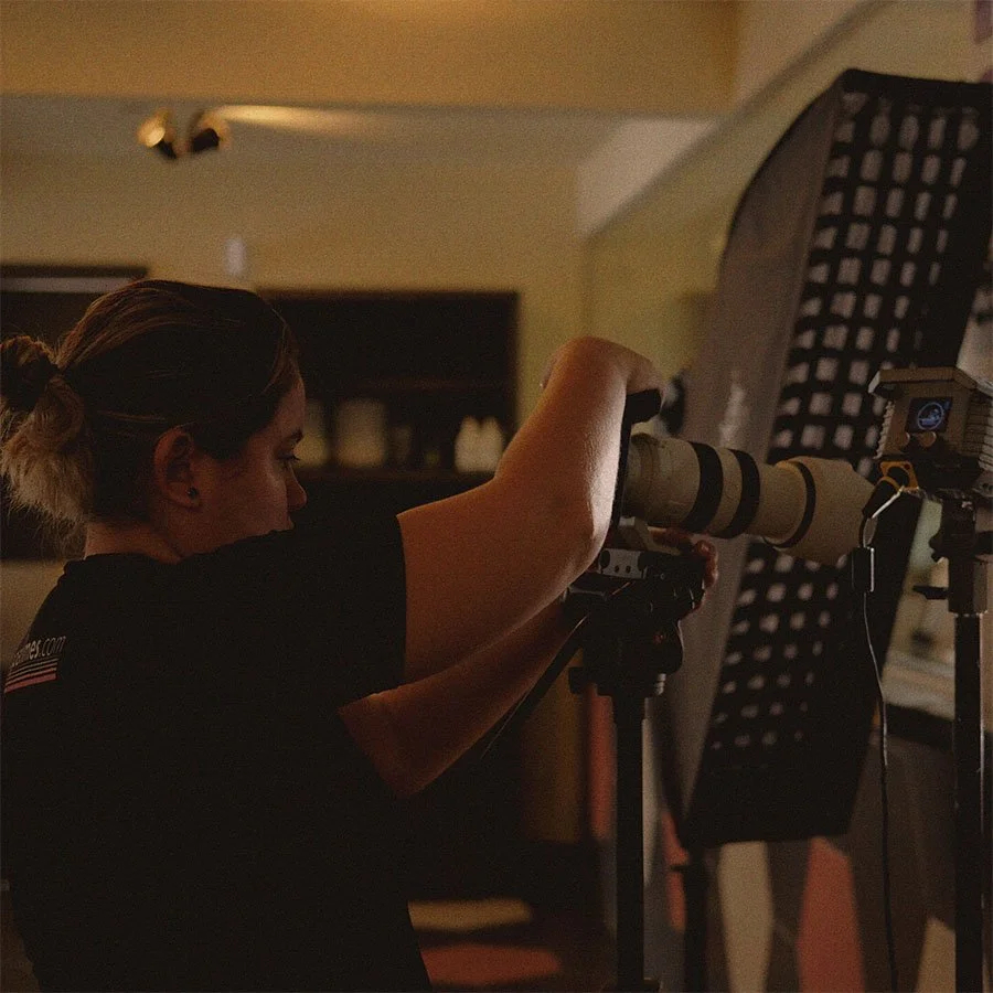 Mulher usando uma câmera com lente telephoto em um ambiente interno.