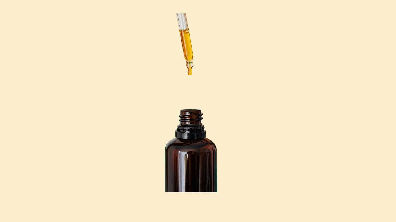 A dropper releasing yellowish liquid into the opening of a brown glass bottle against a light beige background.