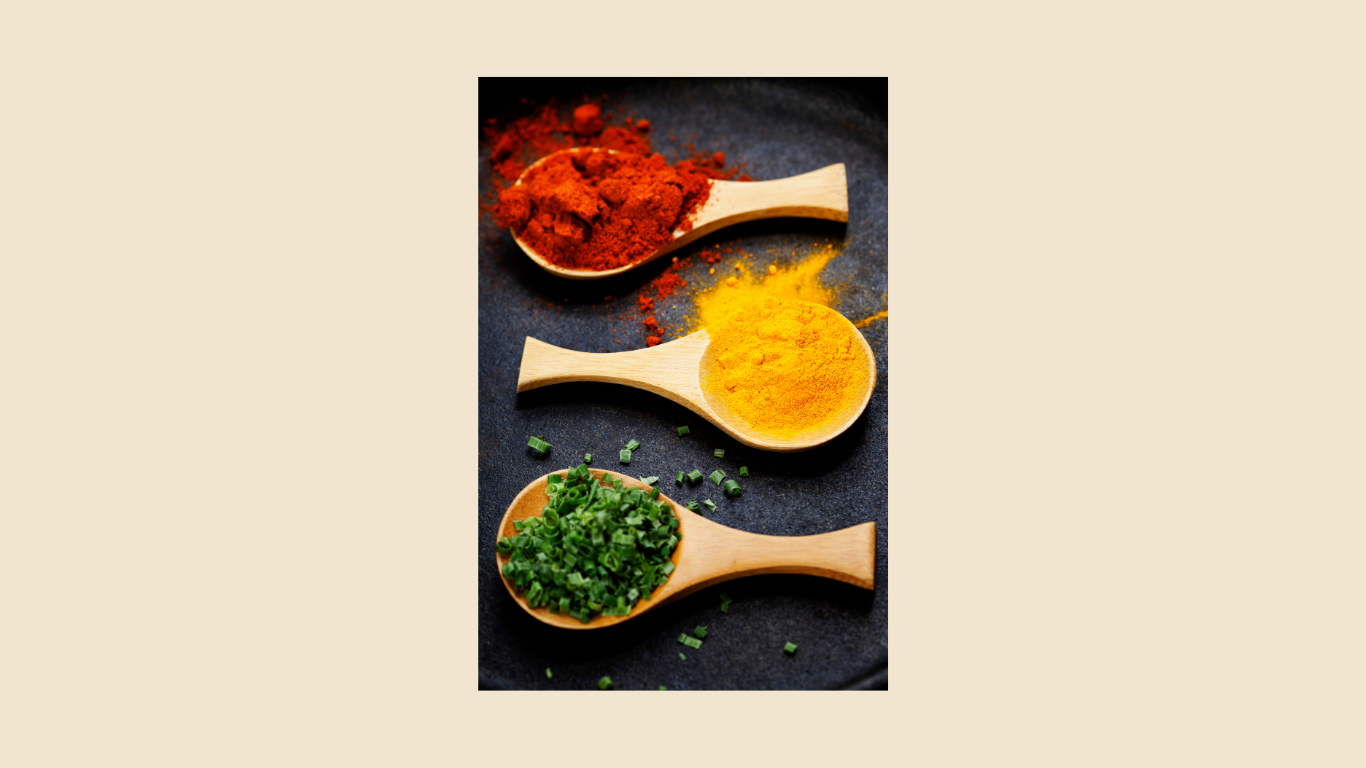Three wooden spoons filled with different spices and herbs, including red paprika, yellow turmeric, and chopped green onions.