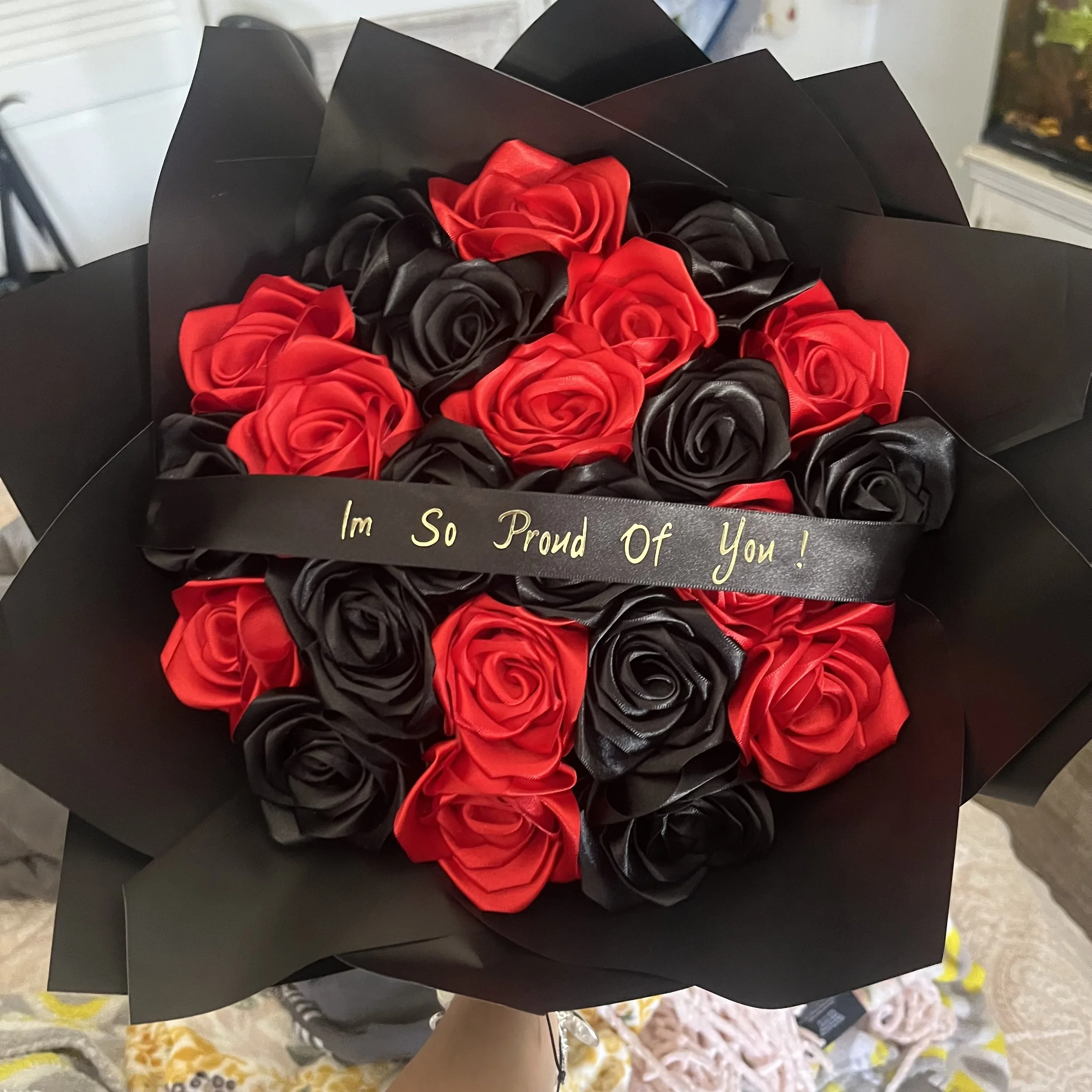 Bouquet of artificial red and black roses wrapped in black paper with a black ribbon that says "I'm So Proud Of You!"