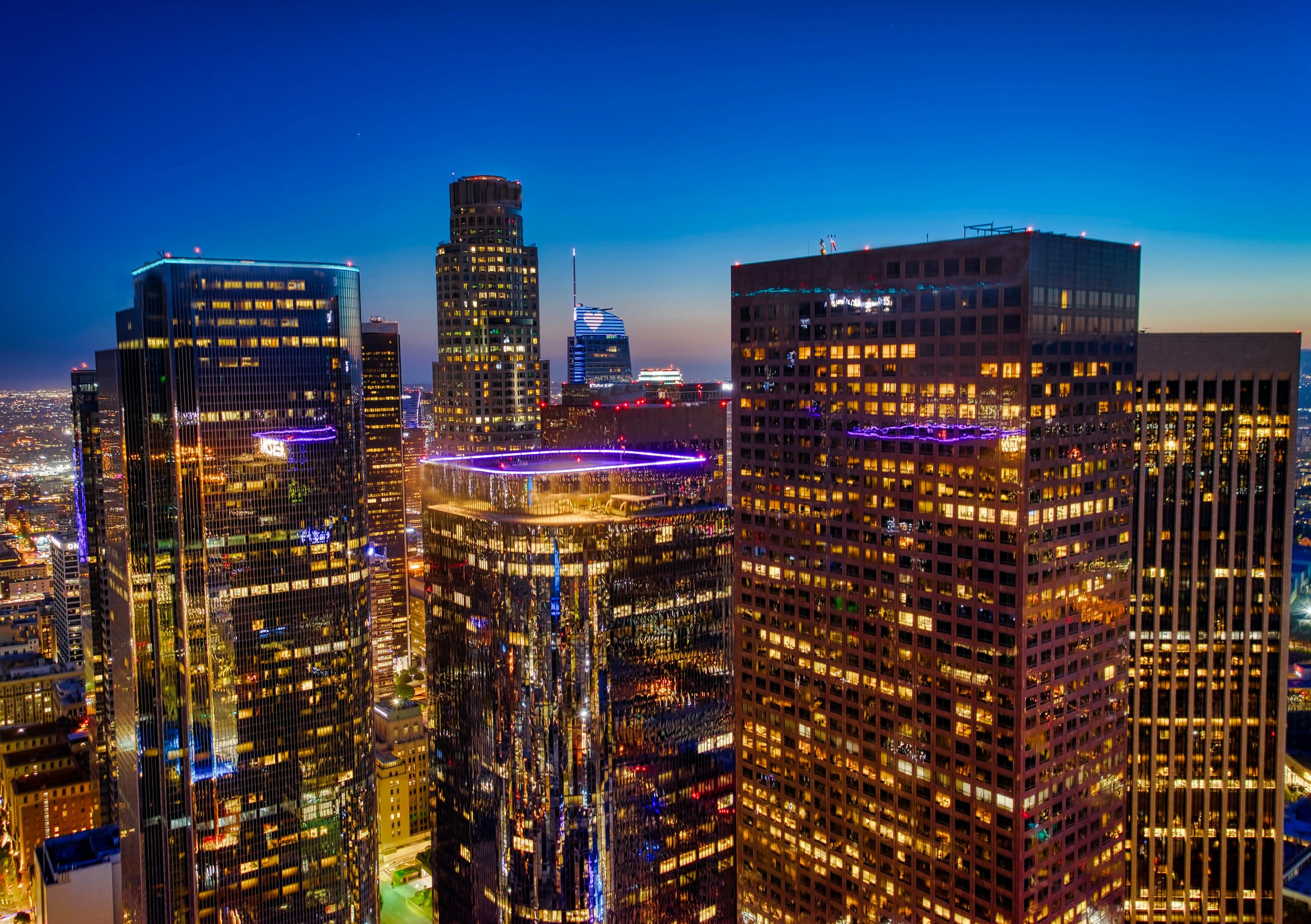Nighttime cityscape of downtown Los Angeles with illuminated skyscrapers and buildings reflecting city lights.