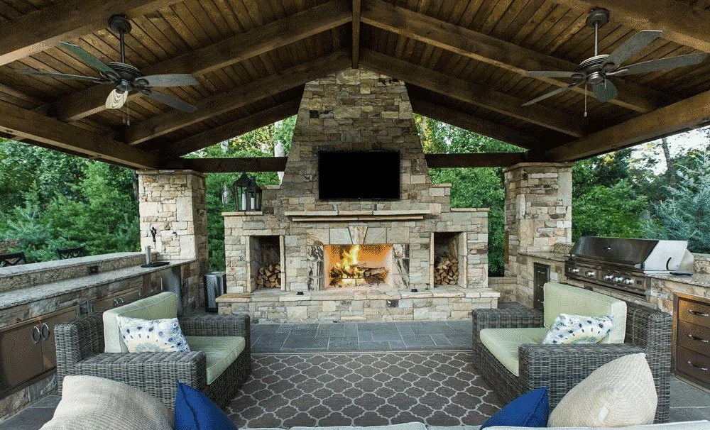 Outdoor covered patio with stone fireplace, ceiling fans, seating area, and a built-in grill.