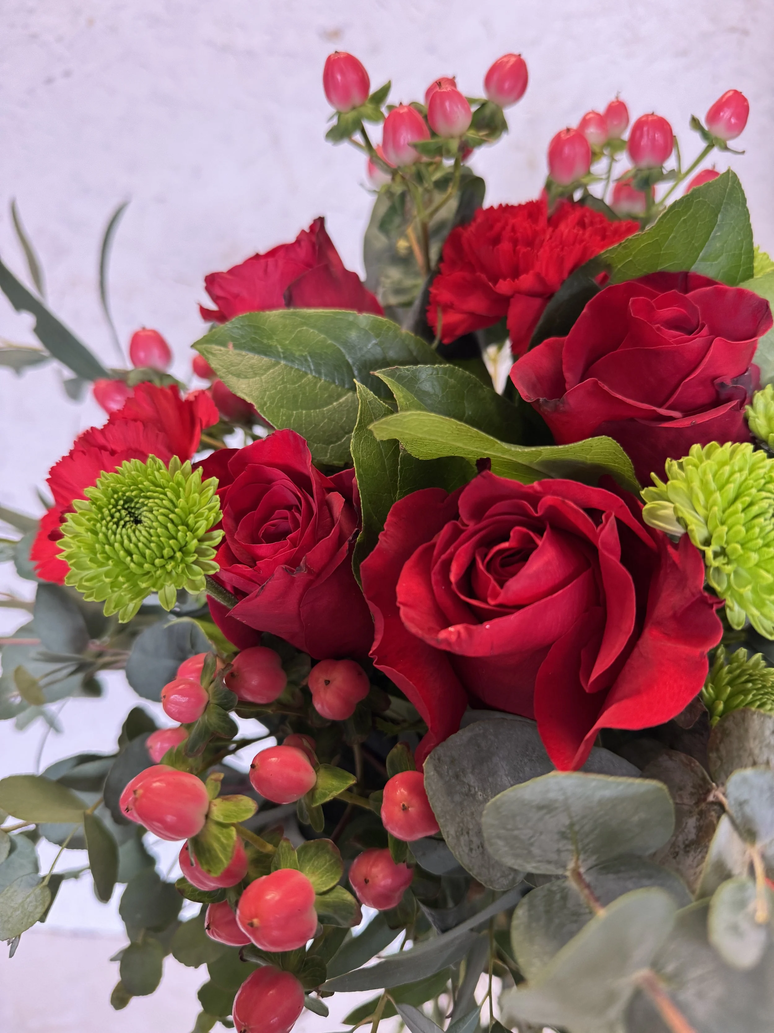 A bouquet of red roses, green chrysanthemums, pink berries, and assorted green leaves arranged together.
