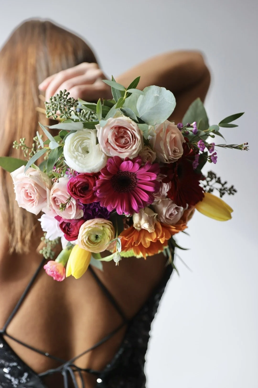 Person holding a colorful bouquet of various flowers including roses, daisies, and lilies, partially covering their face