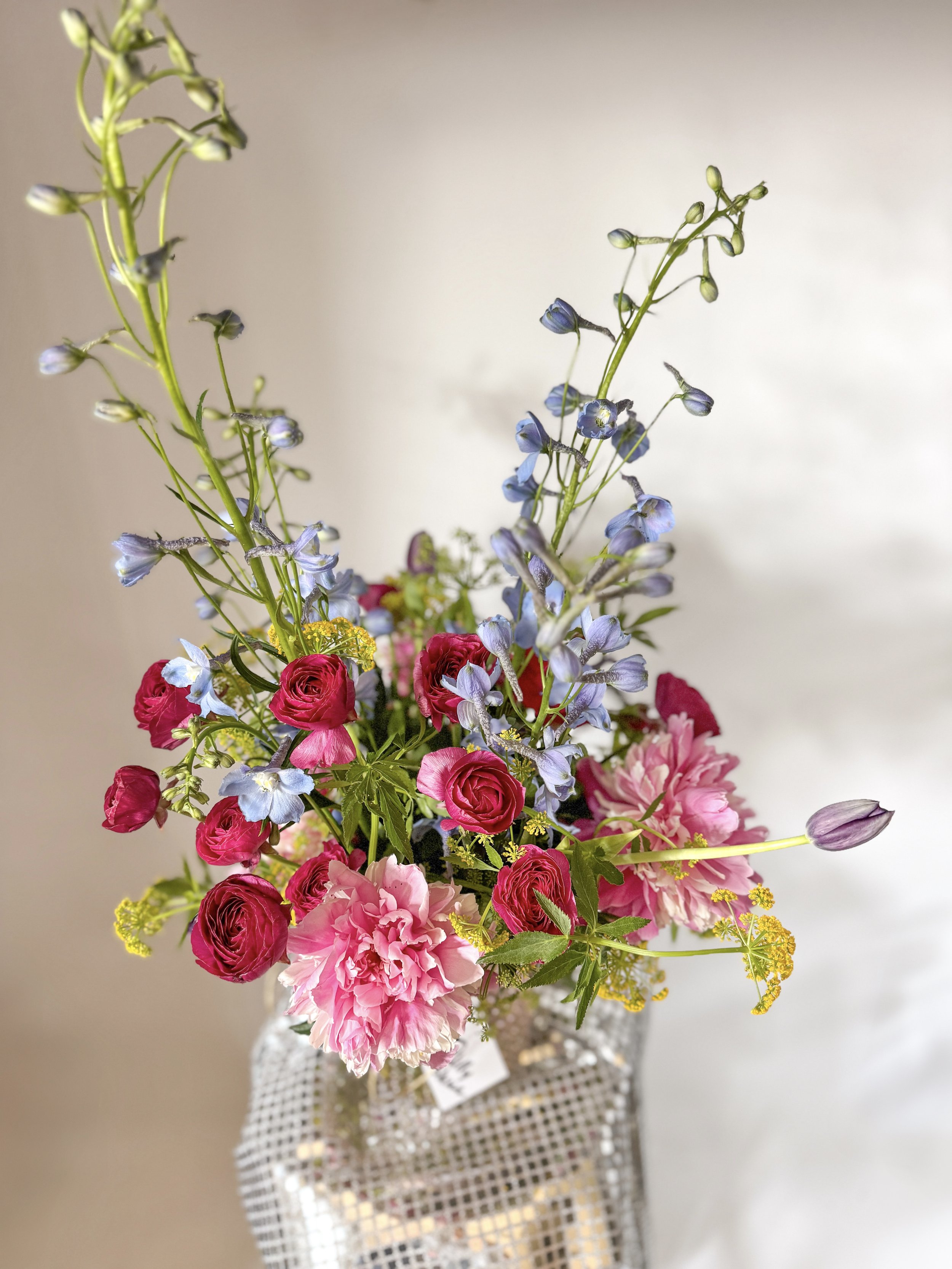 Colorful mixed flower arrangement in a transparent checkered glass vase.