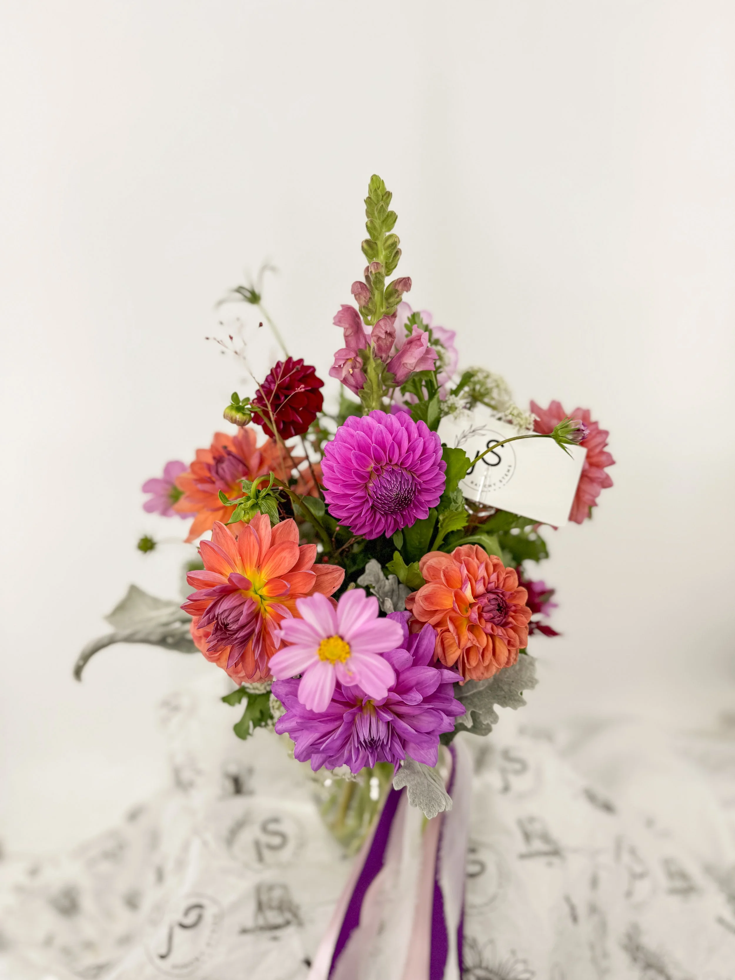 Colorful bouquet of various flowers in a glass vase with a white background.