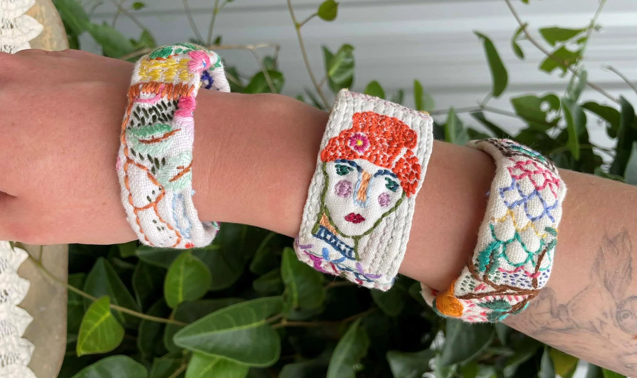 three brightly coloured hand embroidered bangles made from pre-loved table linen are displayed on a forearm