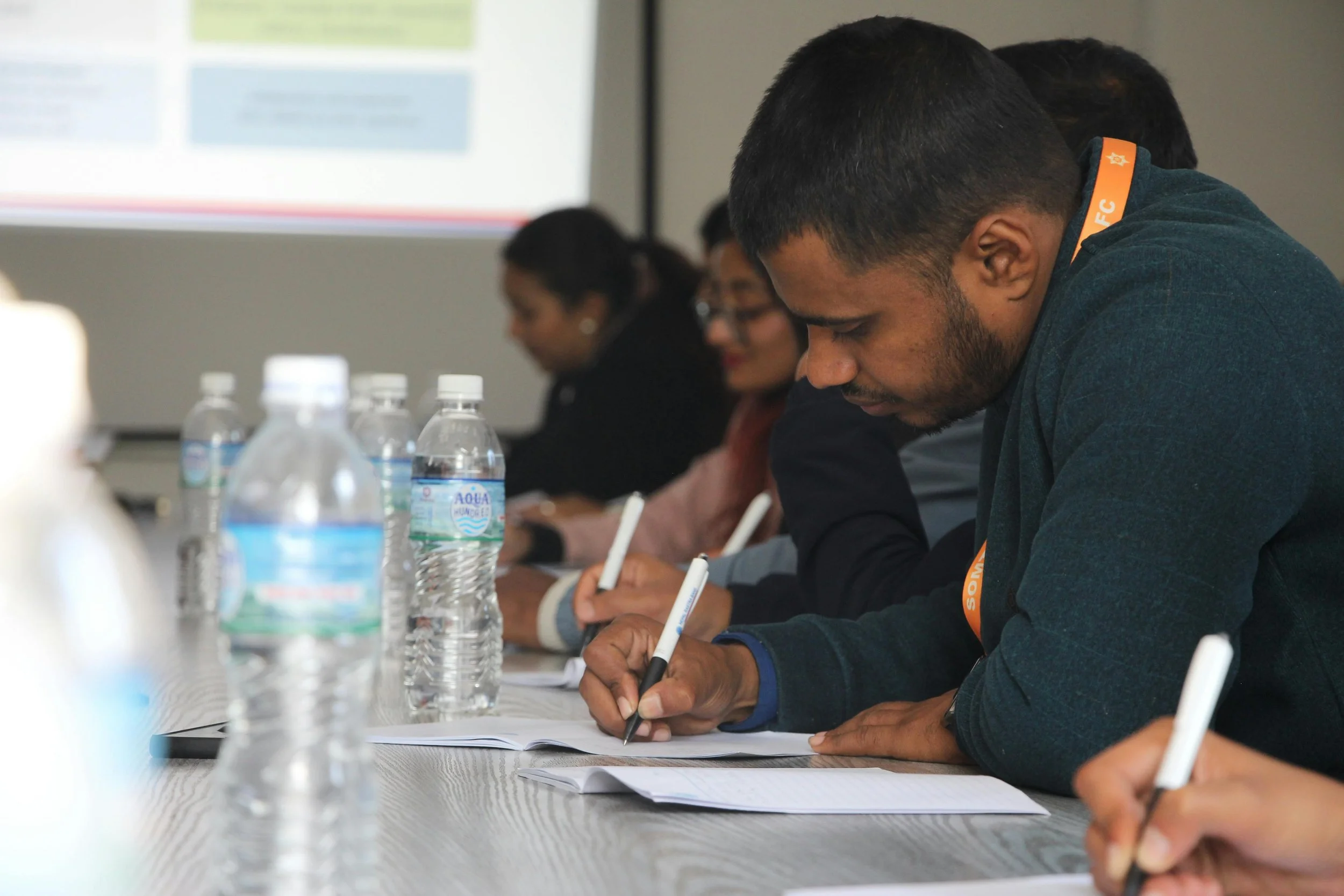 A group of people sits around a table writing with a presentation in the background