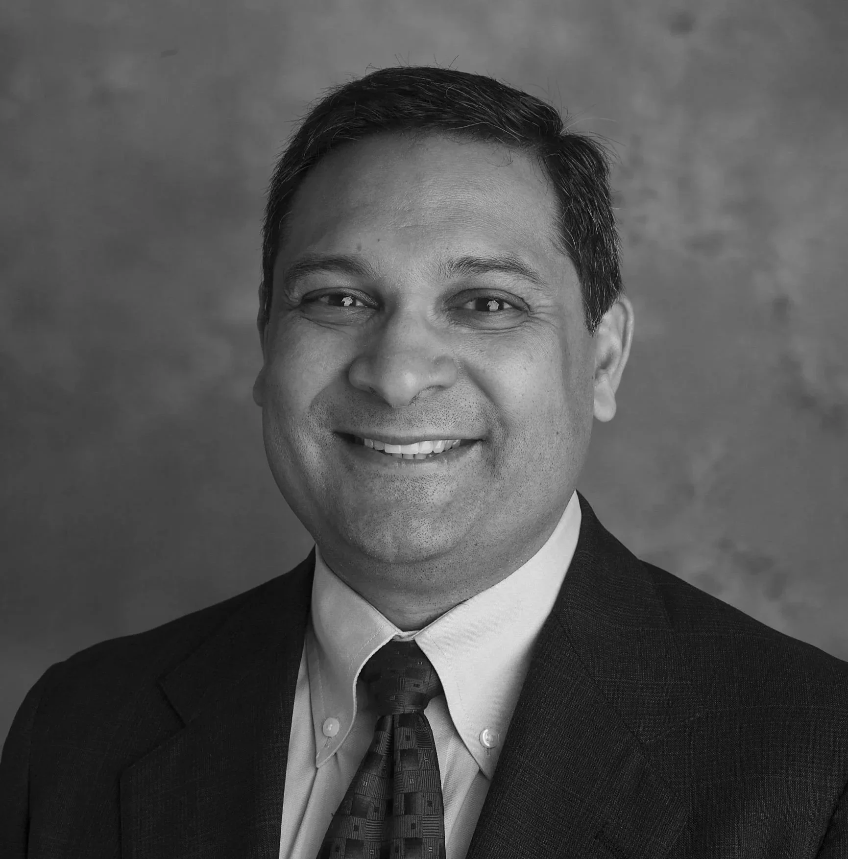 Black and white professional headshot of a smiling man in a suit and tie.