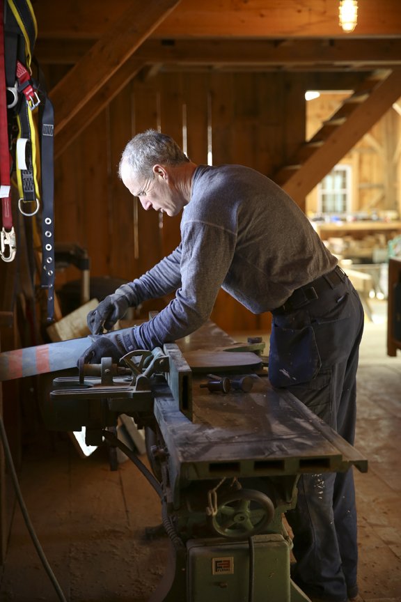 A man working with a saw on a wooden piece in a woodworking shop.