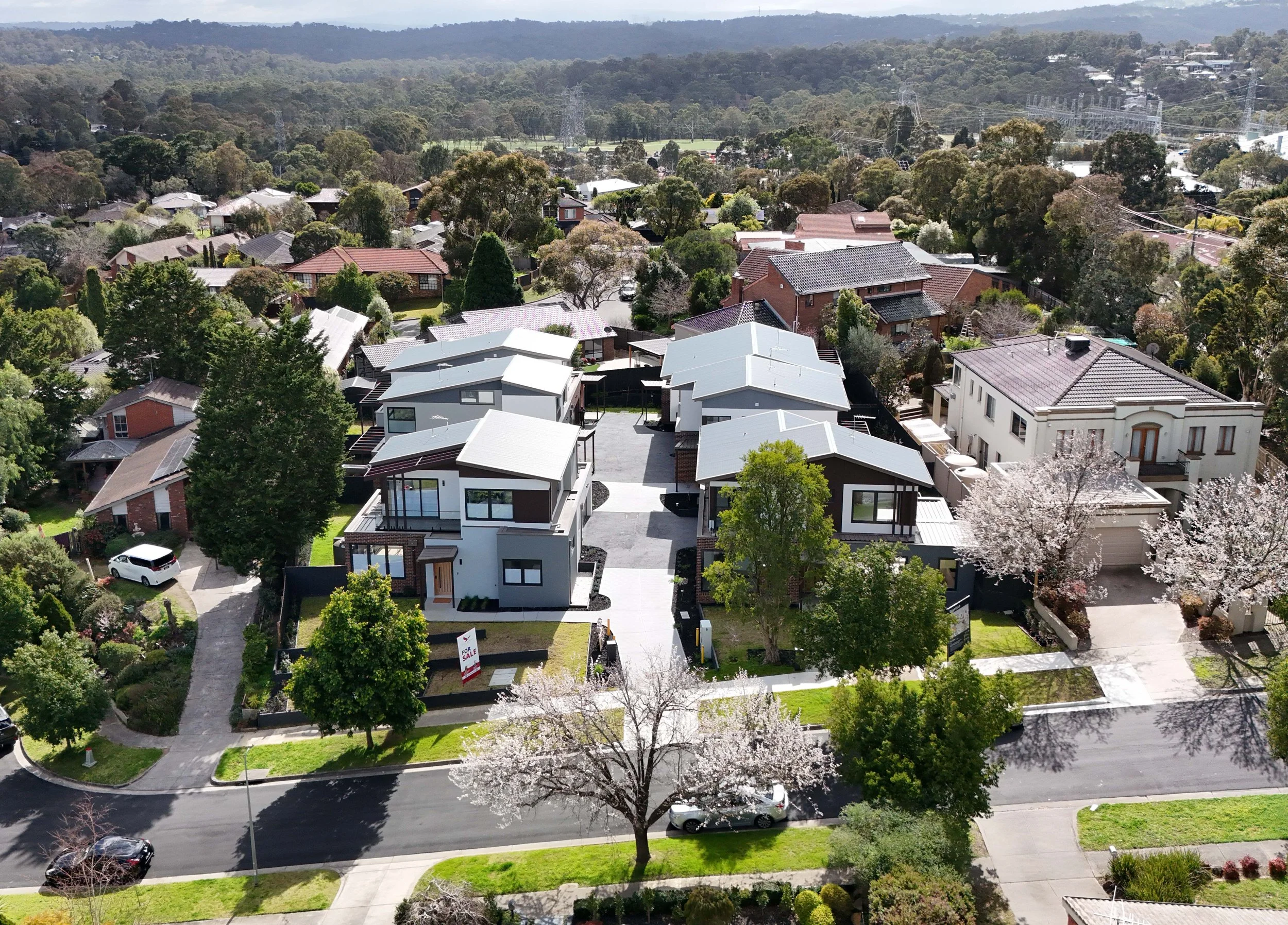 Aerial view of a suburban neighborhood with modern houses, trees, and a street with cars.
