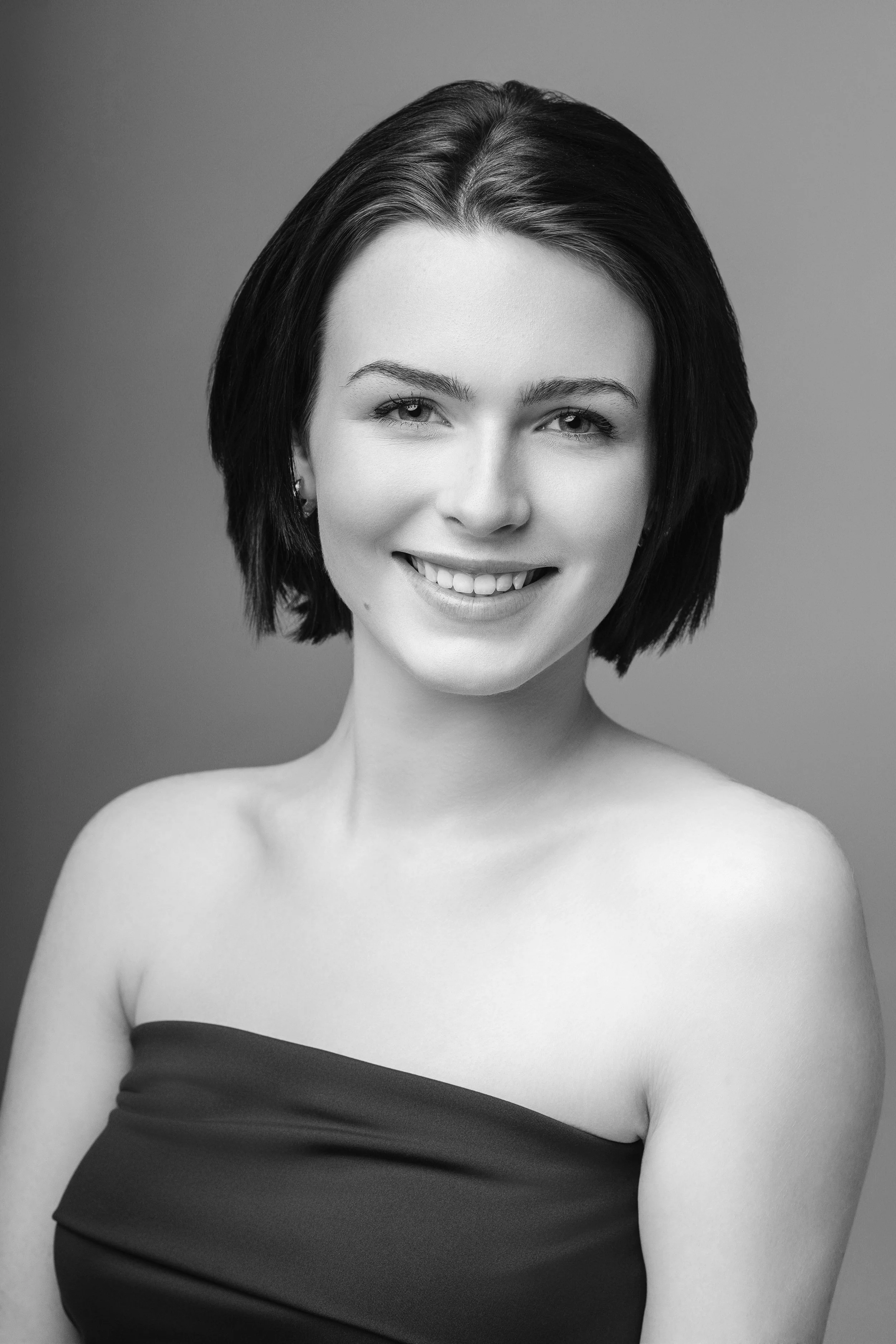 Black and white portrait of a young woman with short dark hair, smiling, wearing a strapless top.