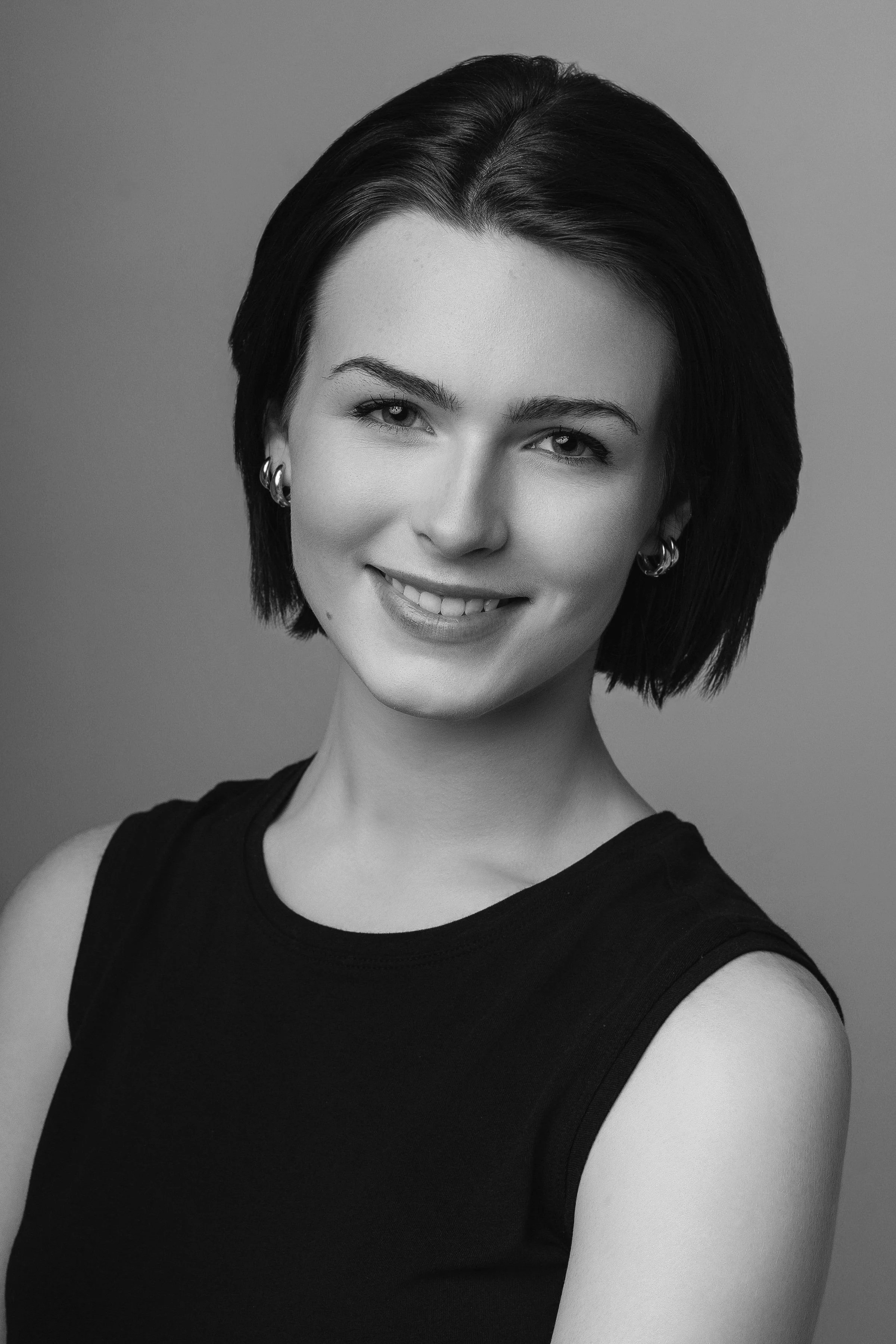 Black-and-white portrait of a smiling young woman with short, dark hair, wearing hoop earrings and a sleeveless top.