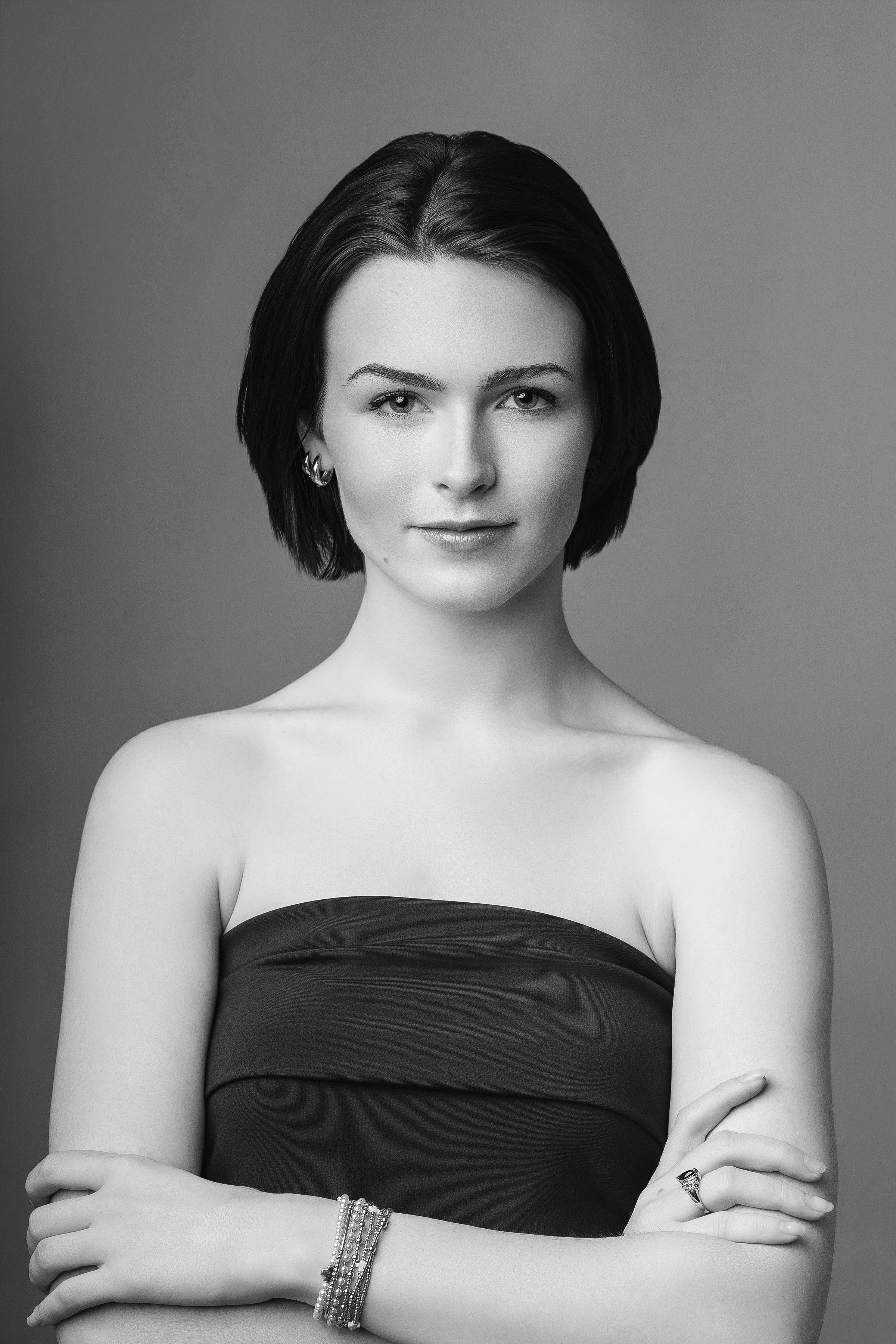 A portrait of a woman with short dark hair, wearing a strapless top and jewelry, facing the camera against a plain background.