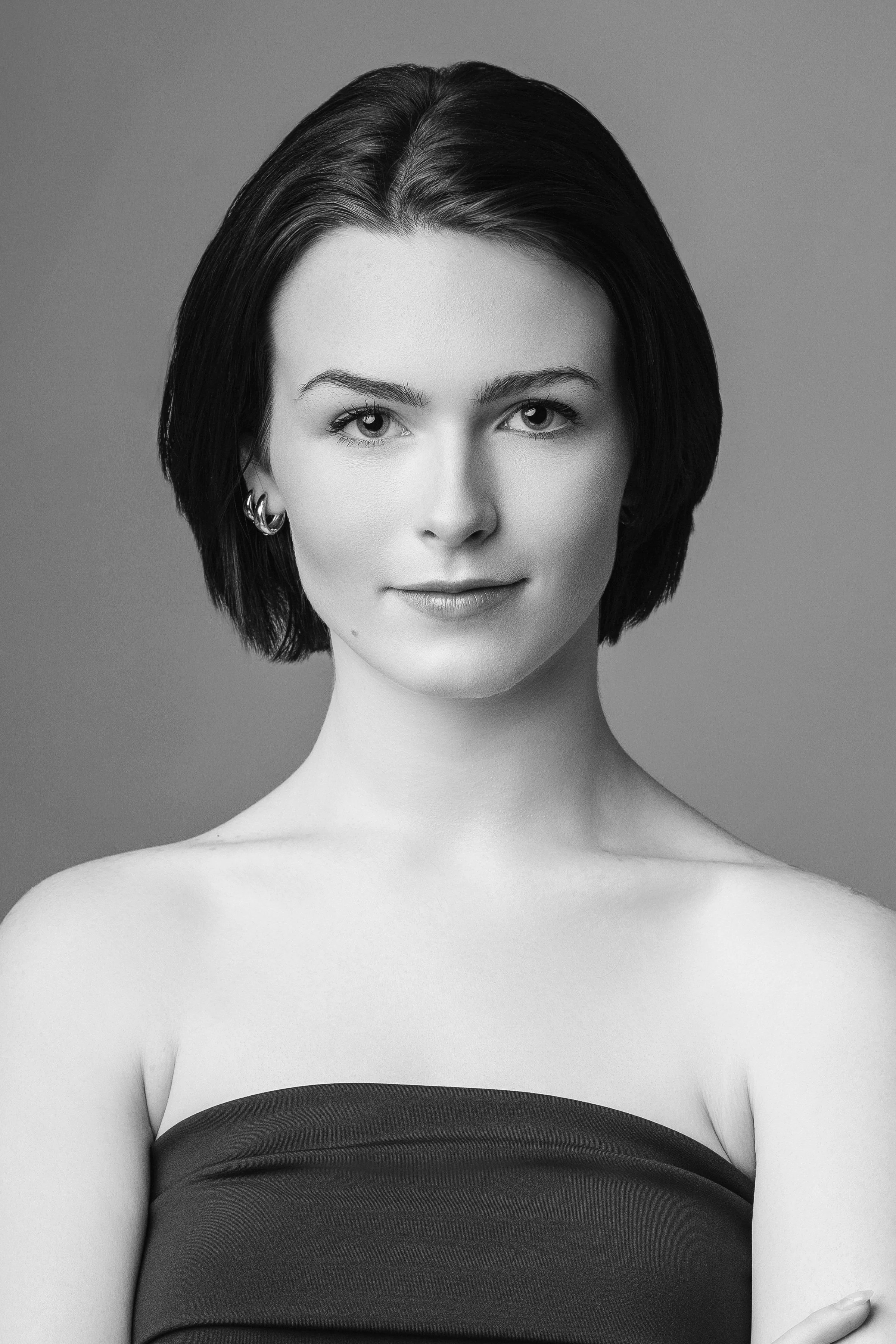 Black and white portrait of a woman with short dark hair, wearing earrings, and a strapless top, smiling slightly.