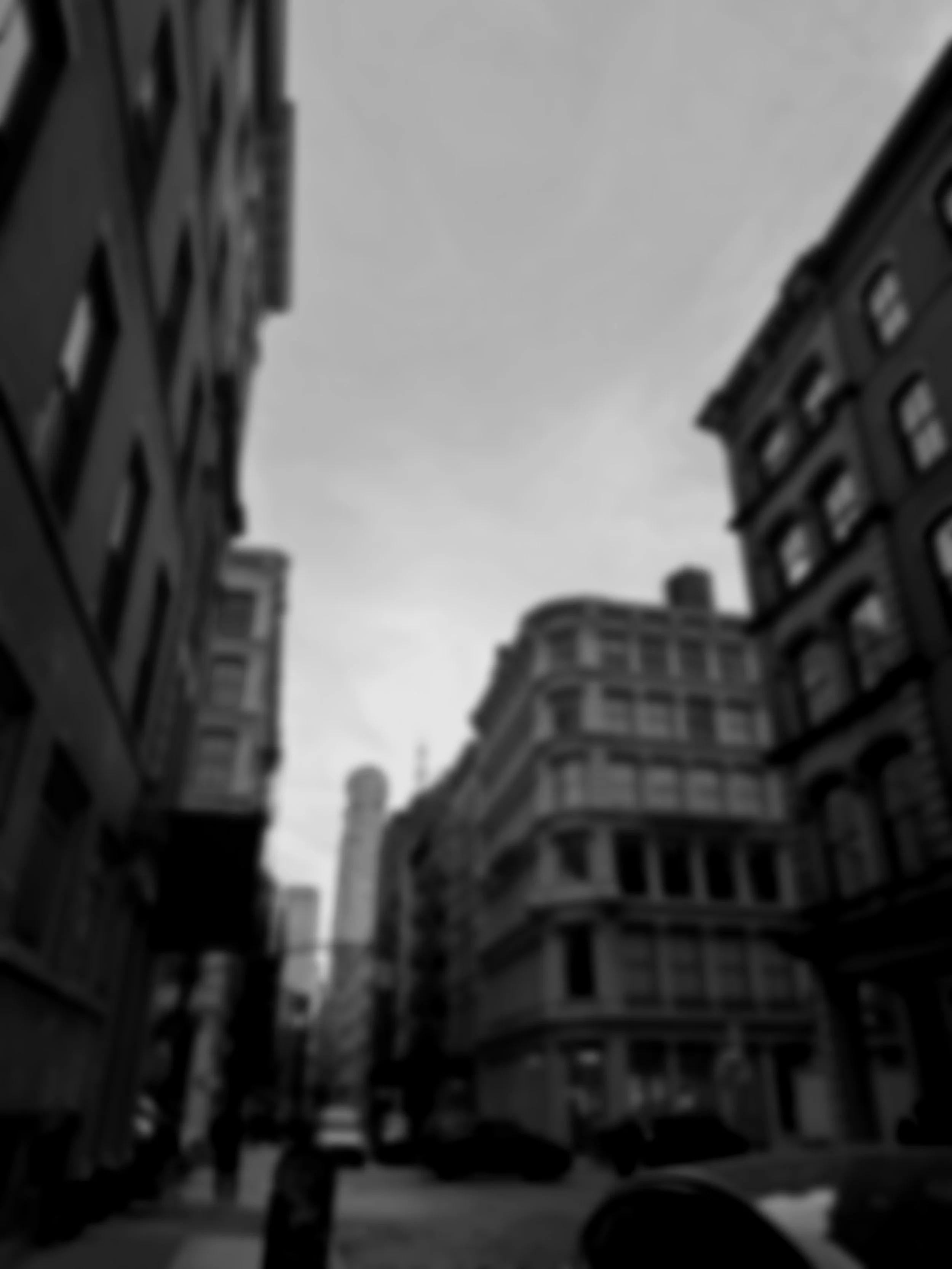 Black and white photo of tall buildings in a city, taken from street level looking up at the sky.