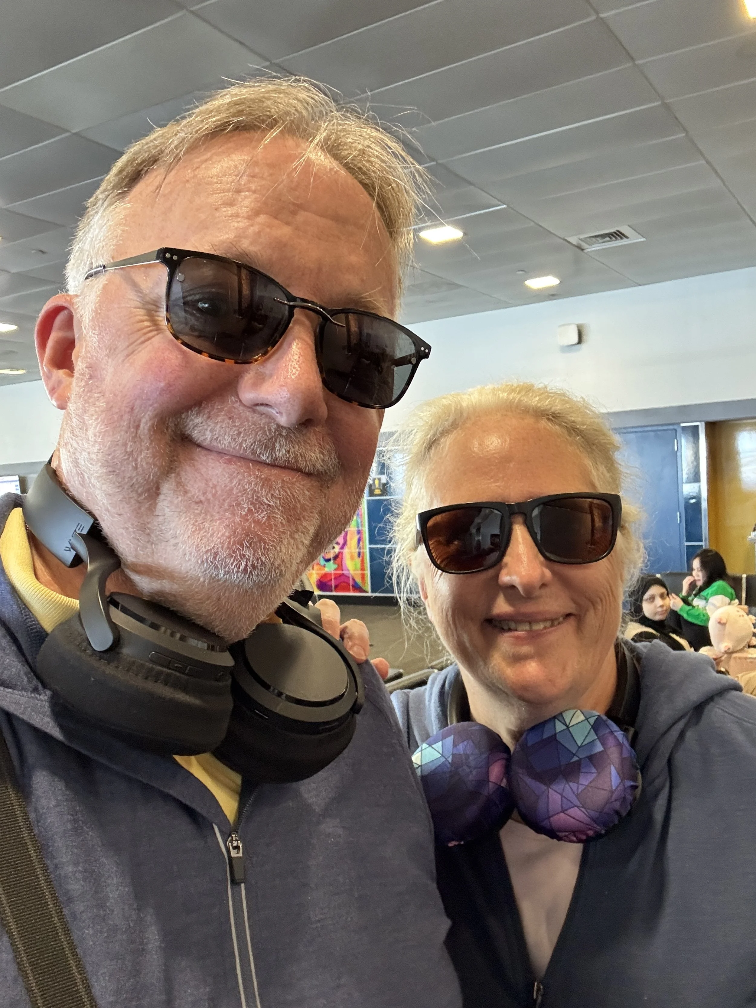 Vinny and Michele wearing sunglasses and wearing wireless headphones around their necks