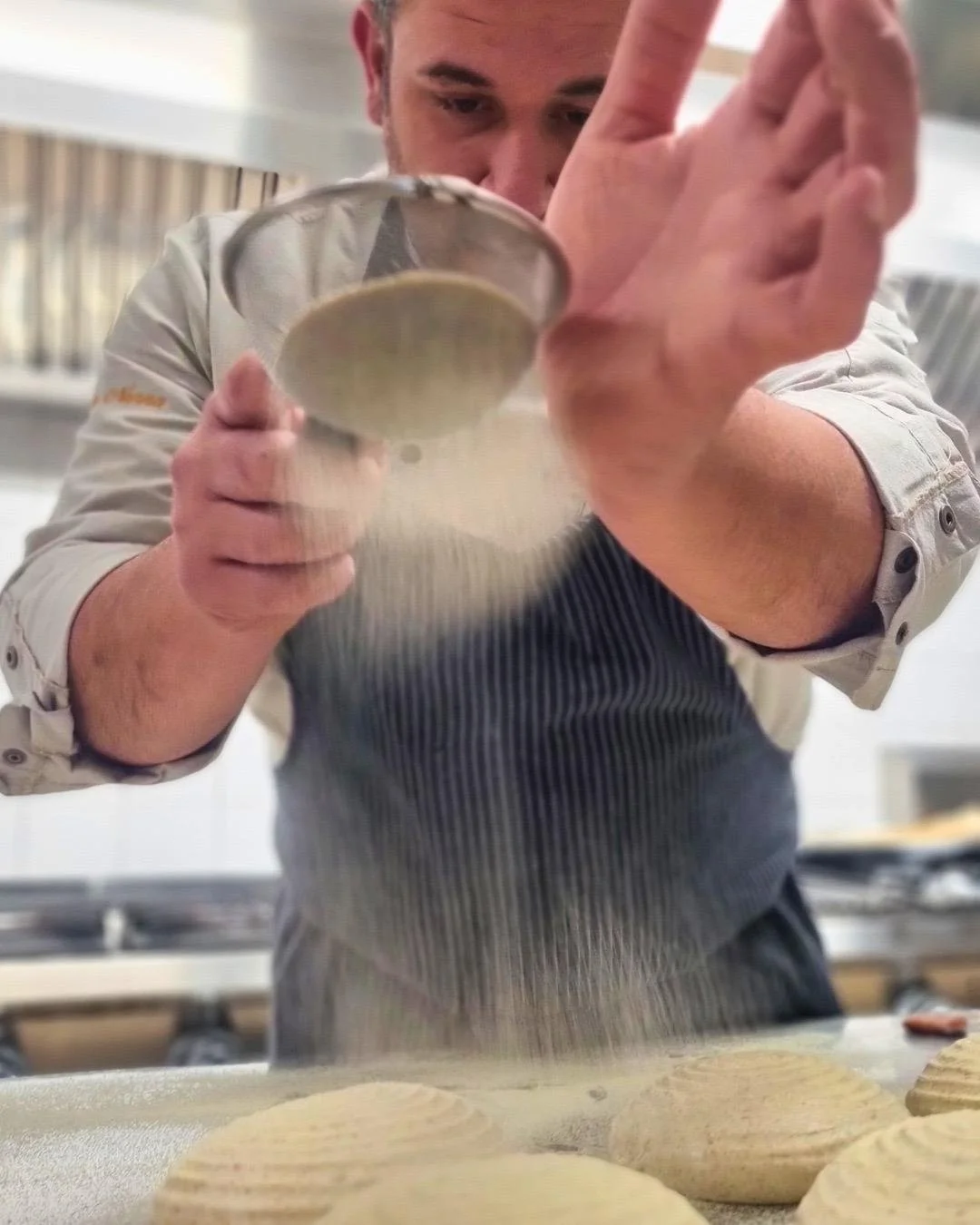 Uno chef che utilizza un setaccio per spolverare farina su dolci in fase di preparazione in cucina.